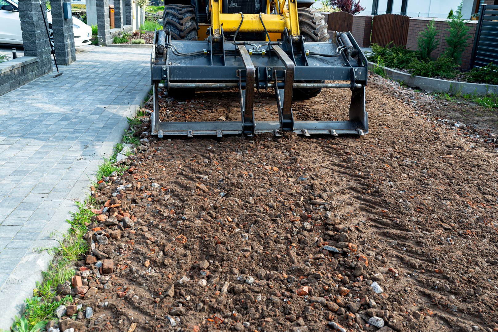 A backhoe loader carries and levels rubble on a dirt road.