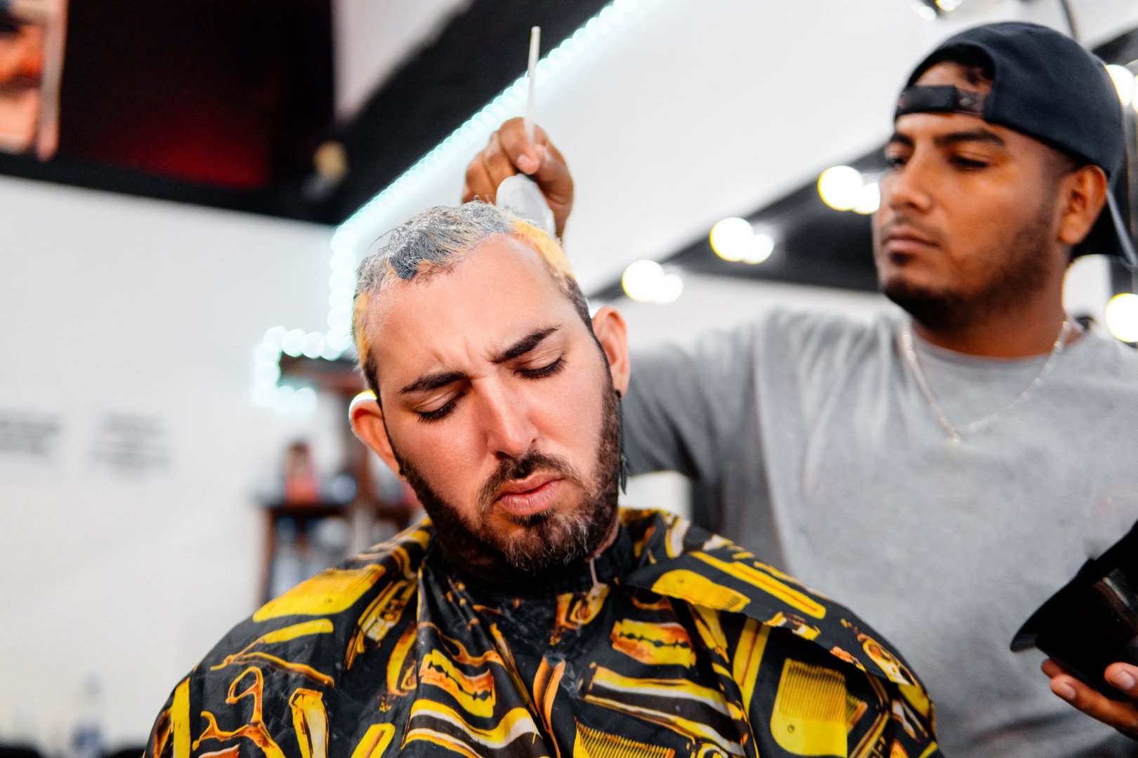 Latin barber applying bleach to a client's hair to dye it in a barbershop