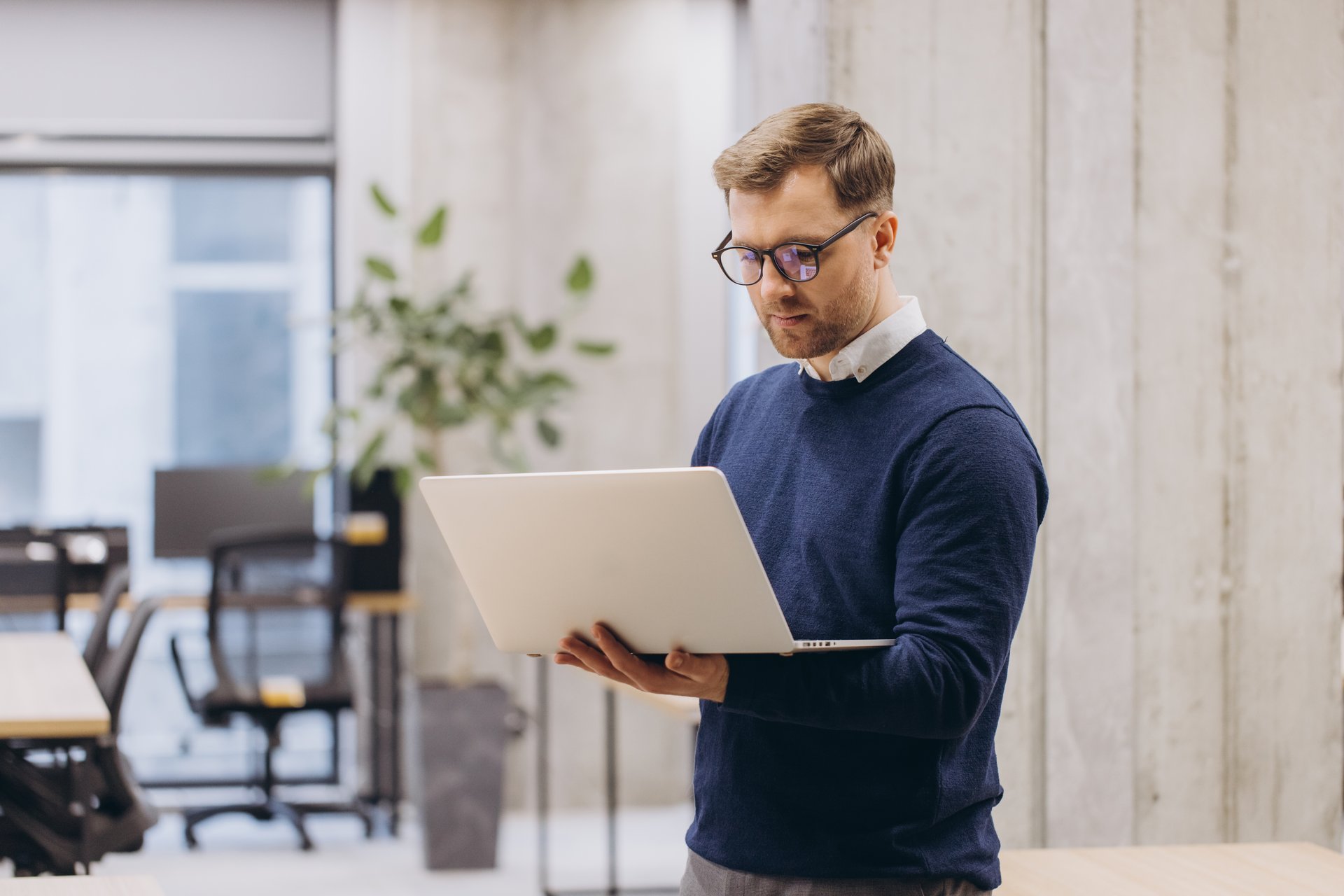 Business professional man using a laptop in a contemporary office setting, focusing on work tasks. Open workspace with natural lighting and plants