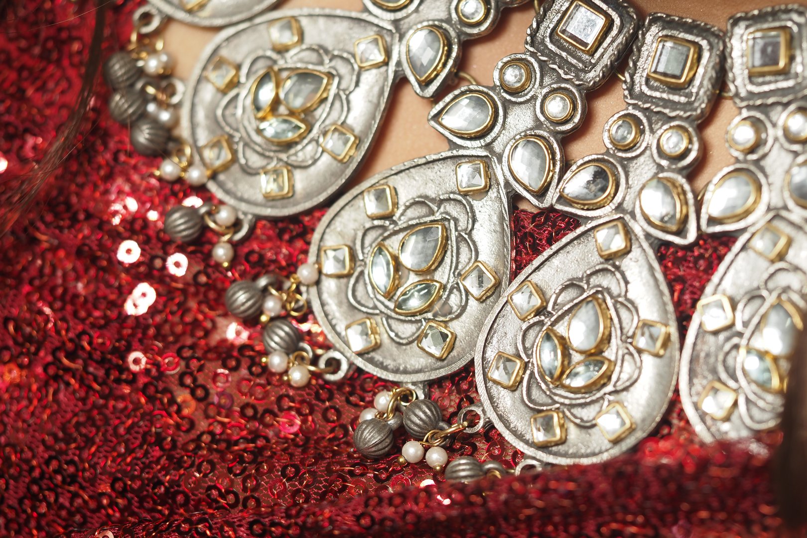 Close view of intricate silver jewelry on vibrant red sequins during an event.