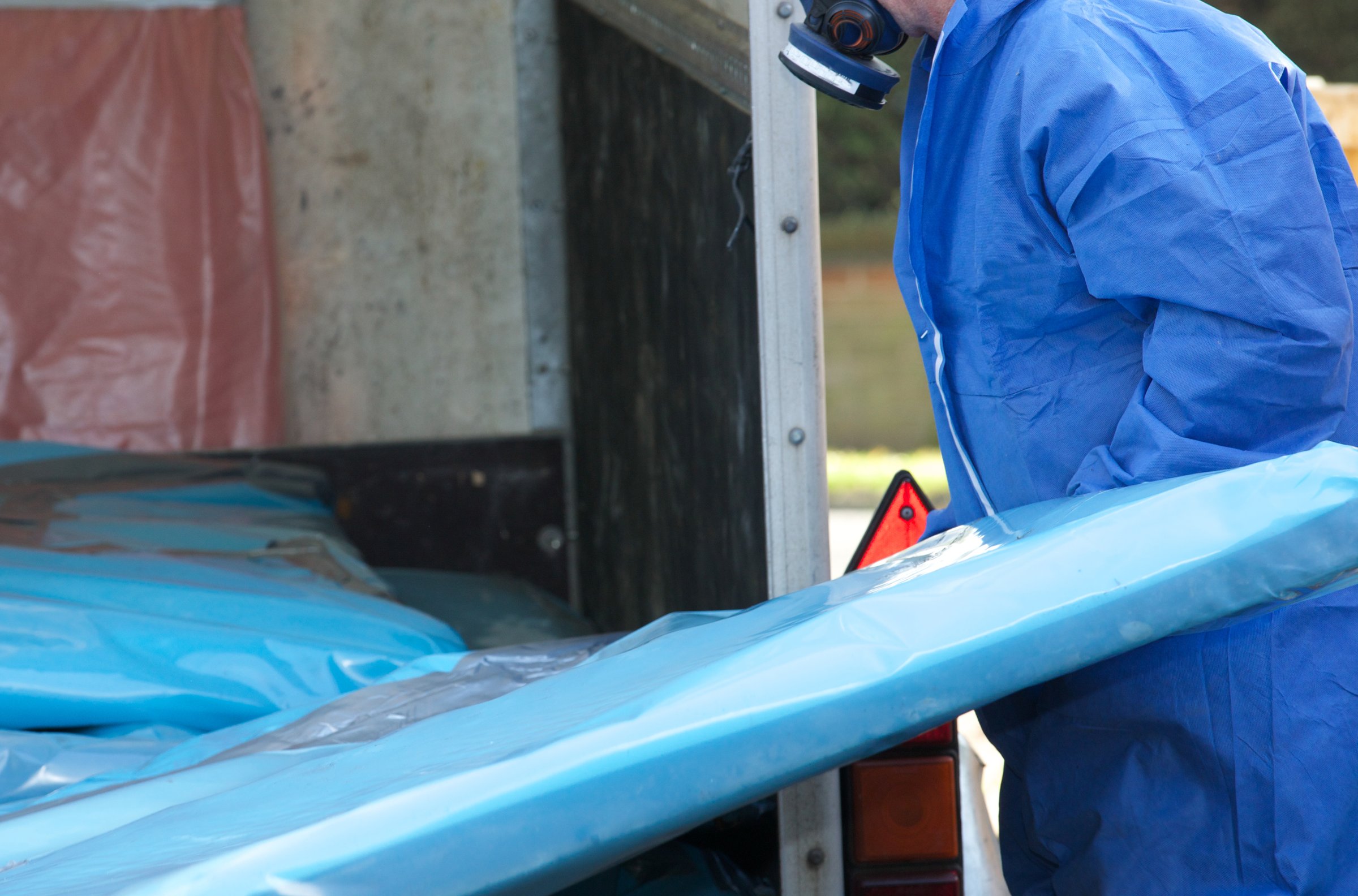 Asbestos corrugated roofing sheet being removed and sealed in a plastic sheet