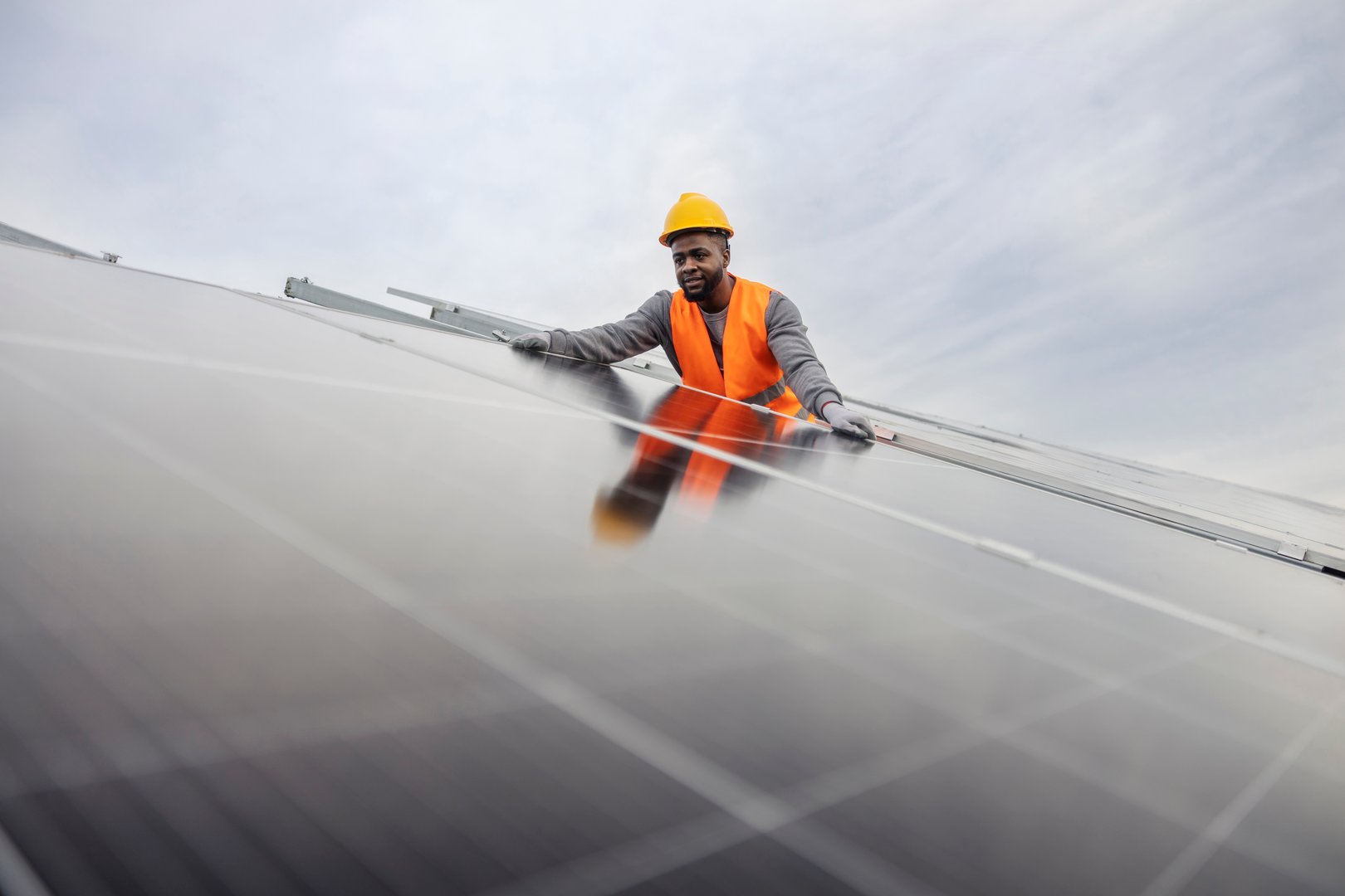 Dedicated interracial migrant worker standing at solar power plant in protective work wear and installing solar panels.