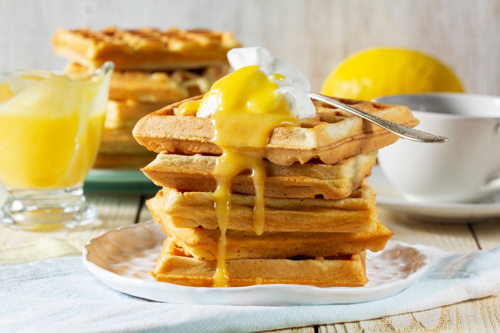 Belgian waffles with cream and lemon curd, served with tea. A traditional treat for carnival. Breakfast of waffles with cream on a light background, rustic style.