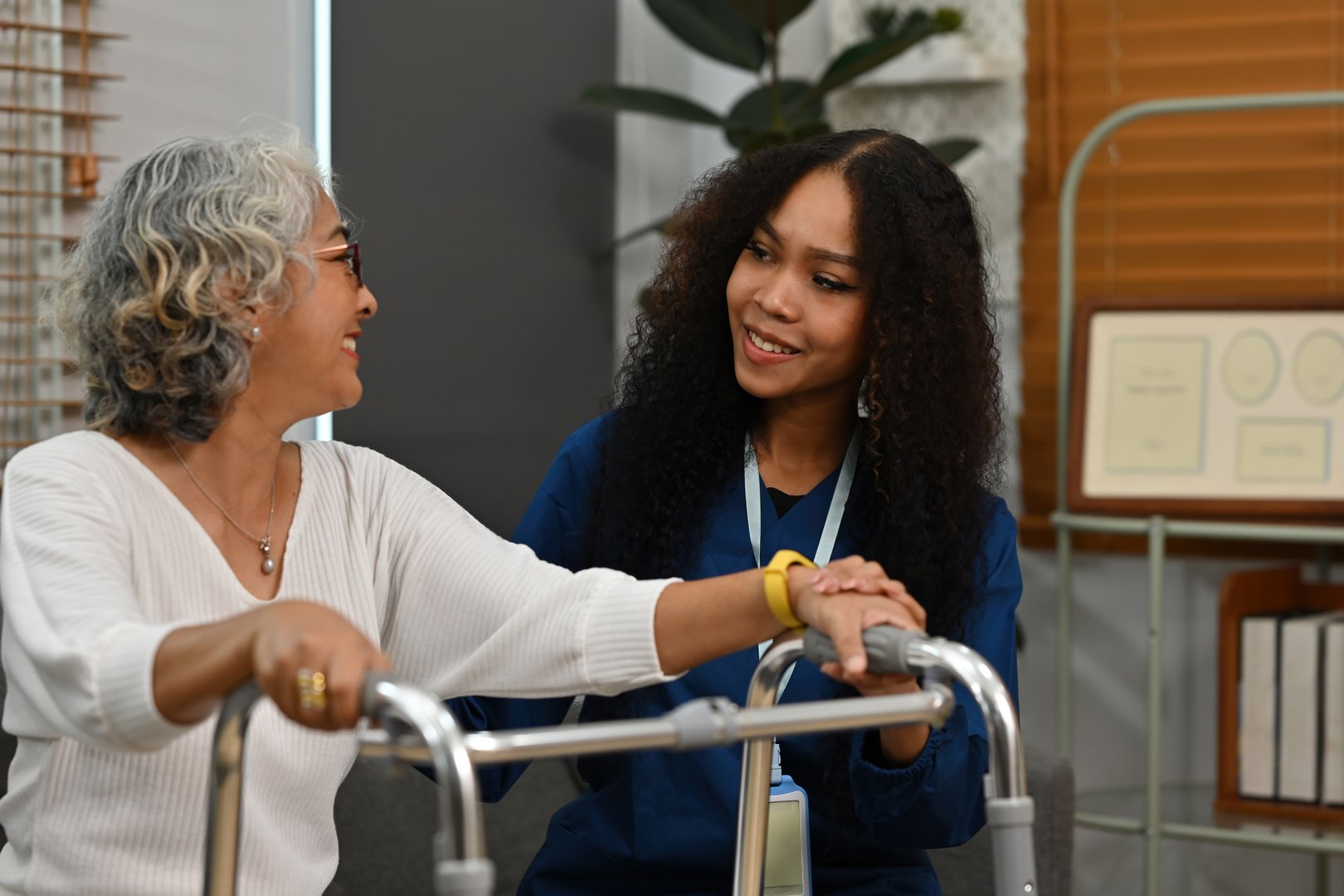 An Afiriacan-Asian young caregiver supports a senior older woman walking in the nursing home. caring for the elderly and doing physical therapy concepts..