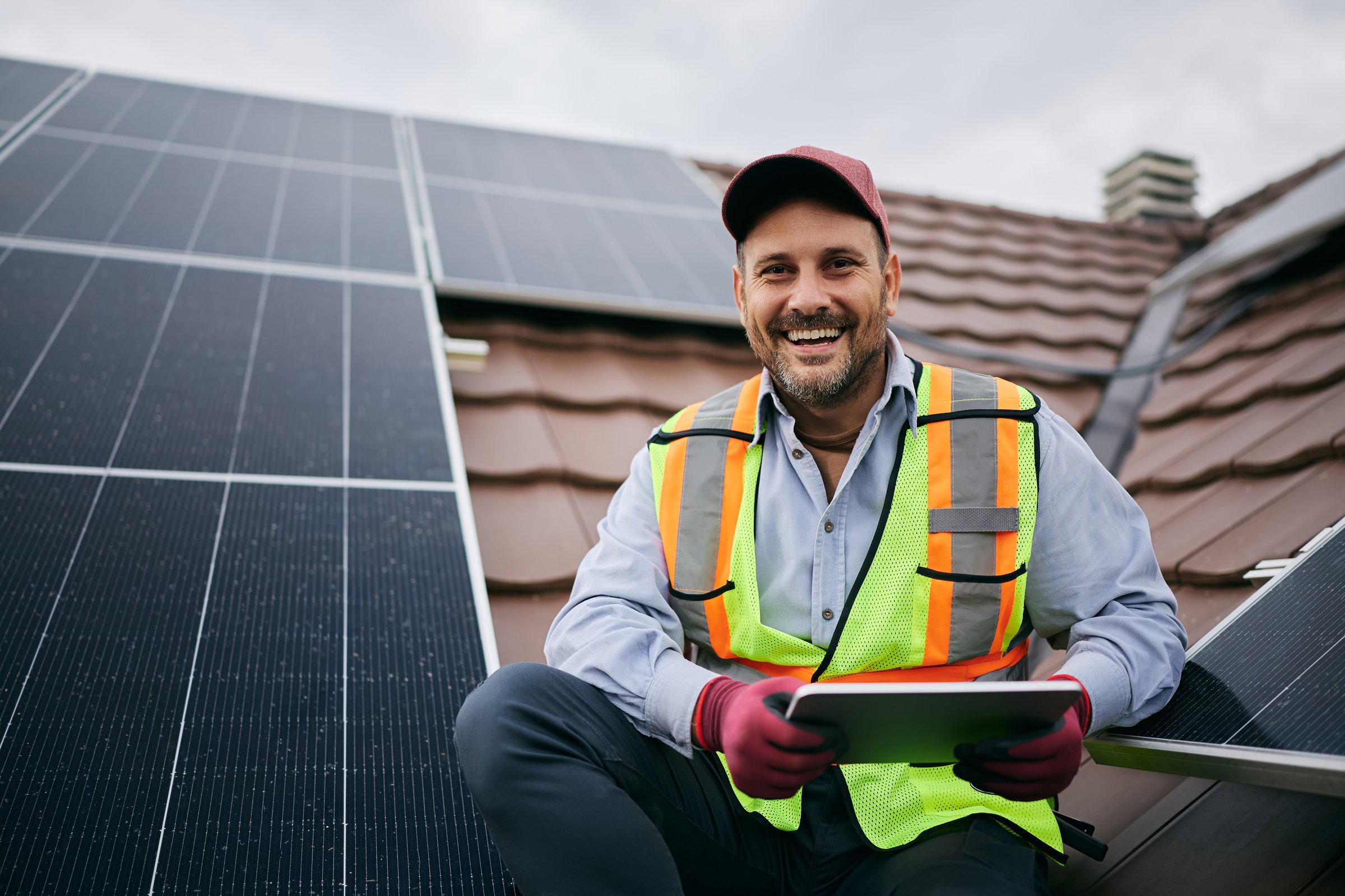 Happy worker using digital tablet during solar panels maintenance and looking at camera.