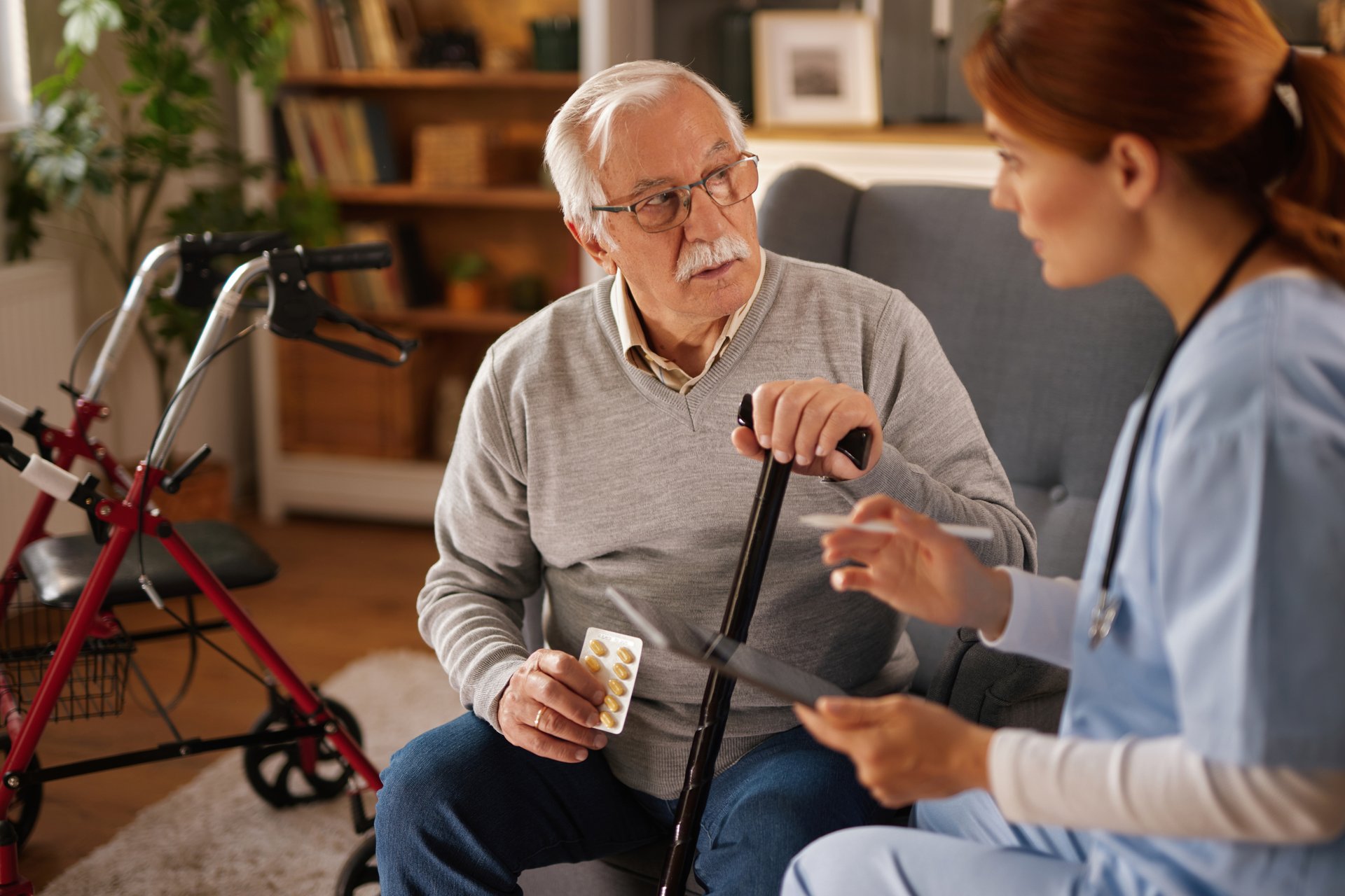 Home caregiver assisting senior man holding his walking stick and explaining his treatment
