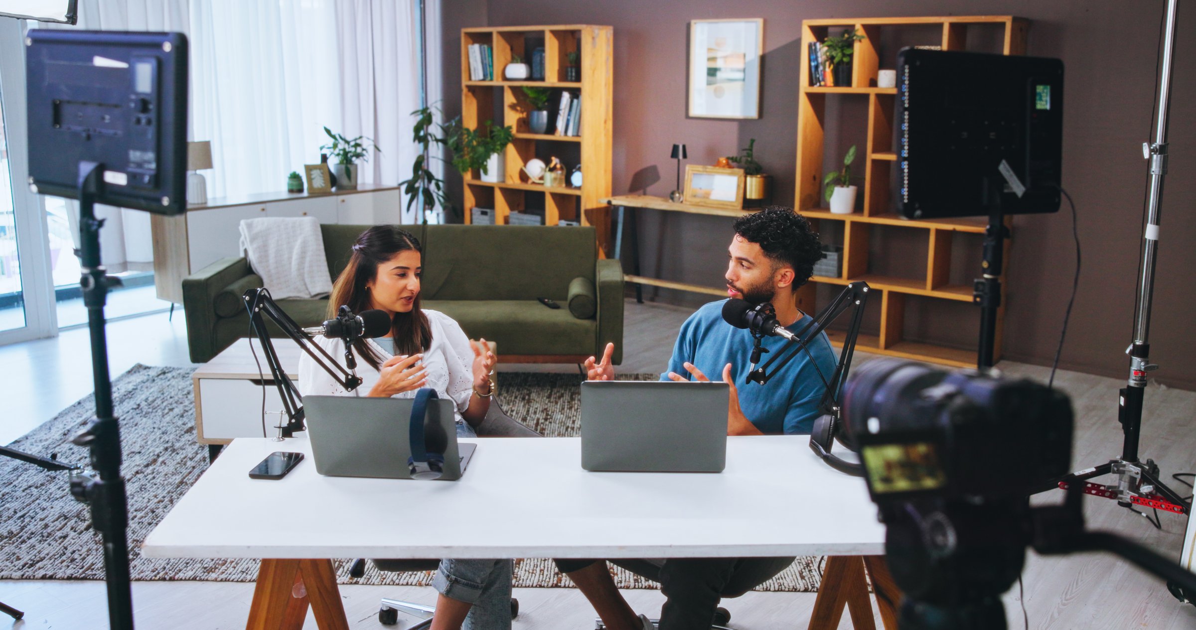 Camera, microphone and podcast with people in home living room for live broadcast or recording. Conversation, laptop or streaming with man and woman influencer in apartment for content creation