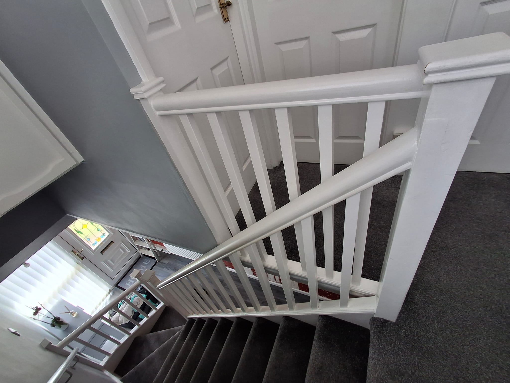 Carpeted staircase with white wooden railings in a home, featuring gray walls and view of entrance door below.