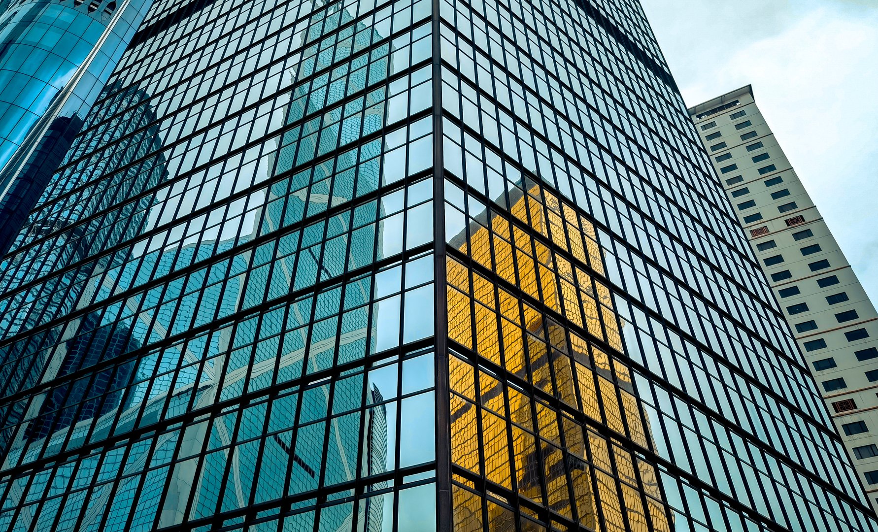 Close-up view of a modern glass building in Hong Kong, reflecting surrounding skyscrapers.