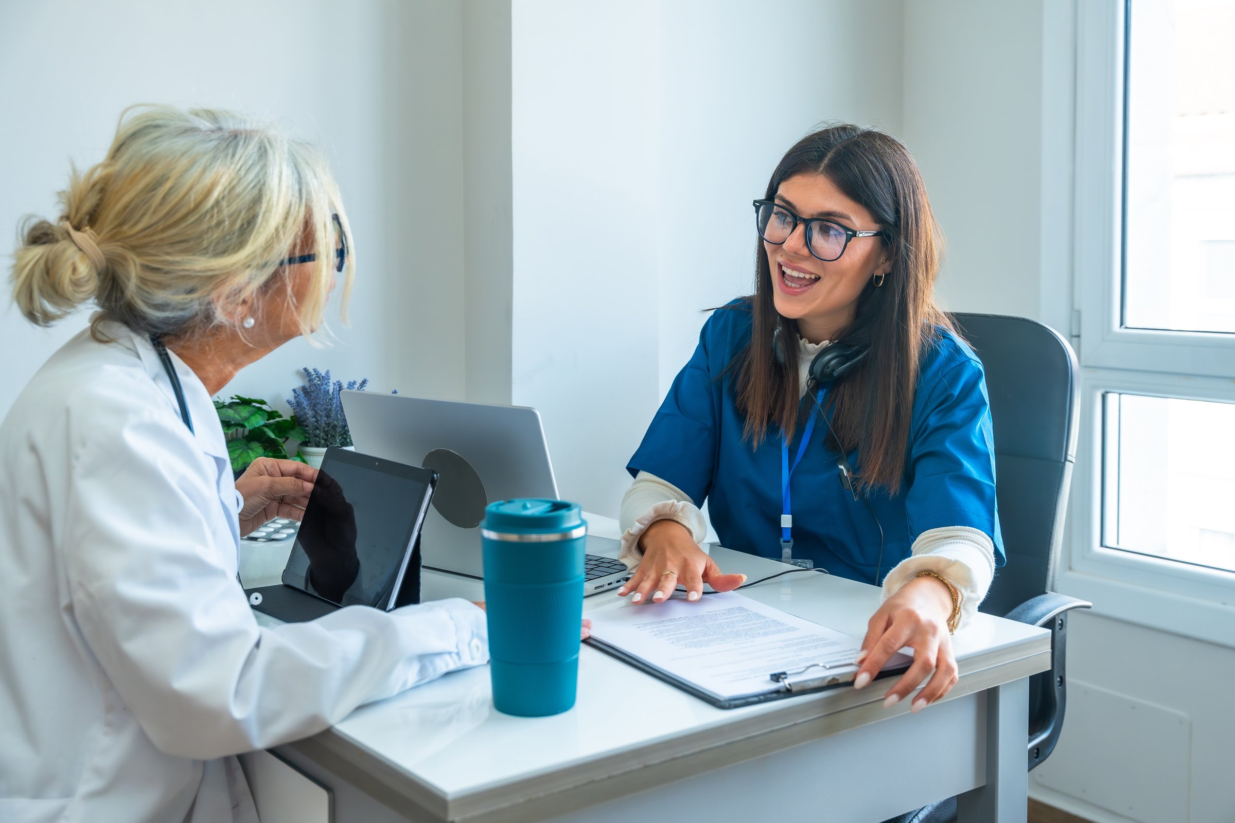 Two women doctors are discussing patient information and medical records, collaborating on healthcare solutions in a professional hospital office setting
