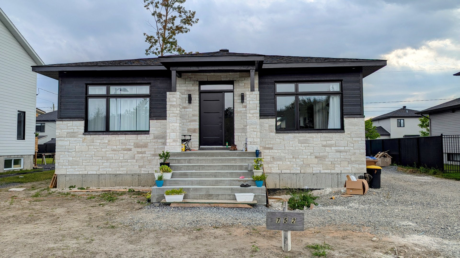 A modern single-story house with stone facade, black trim, wide steps, and a small garden at the entrance.