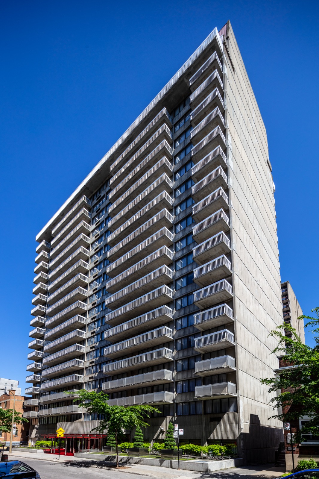 A tall, modern apartment building with balconies viewed from below against a clear blue sky.