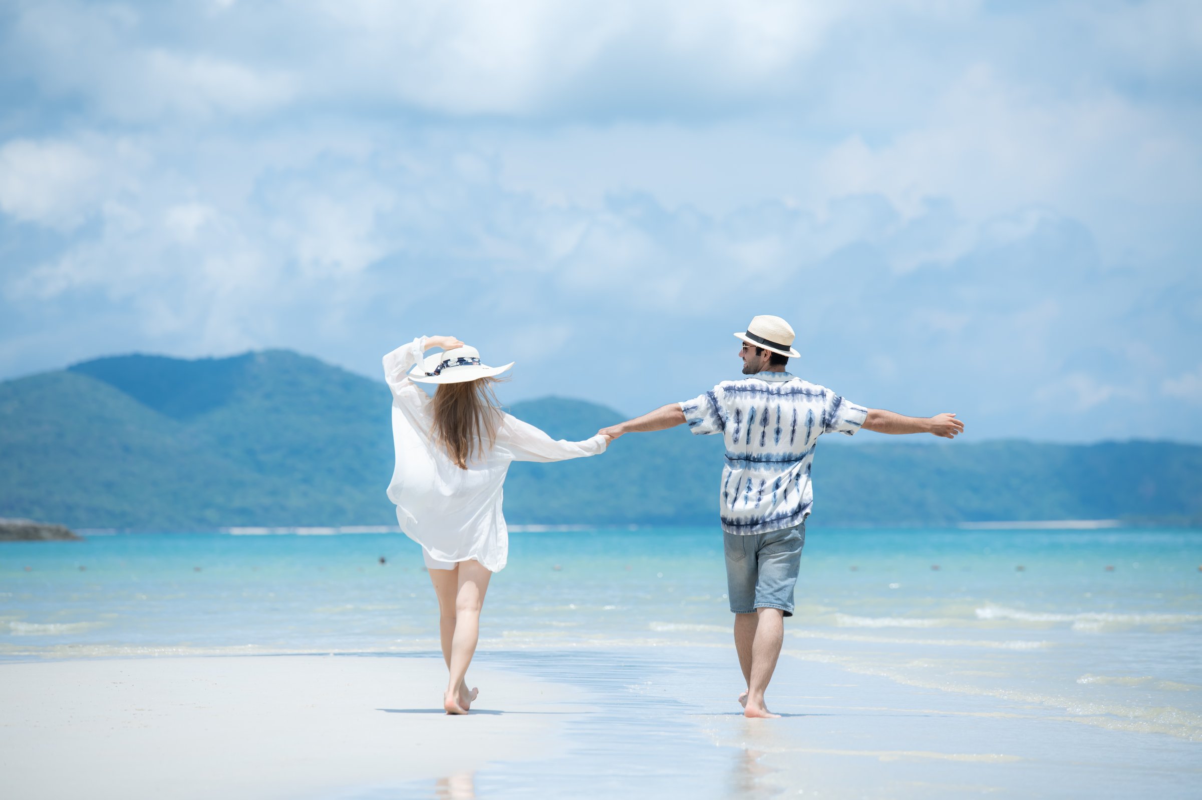 Young couple on vacation on a white sandy beach, clear sky and sea