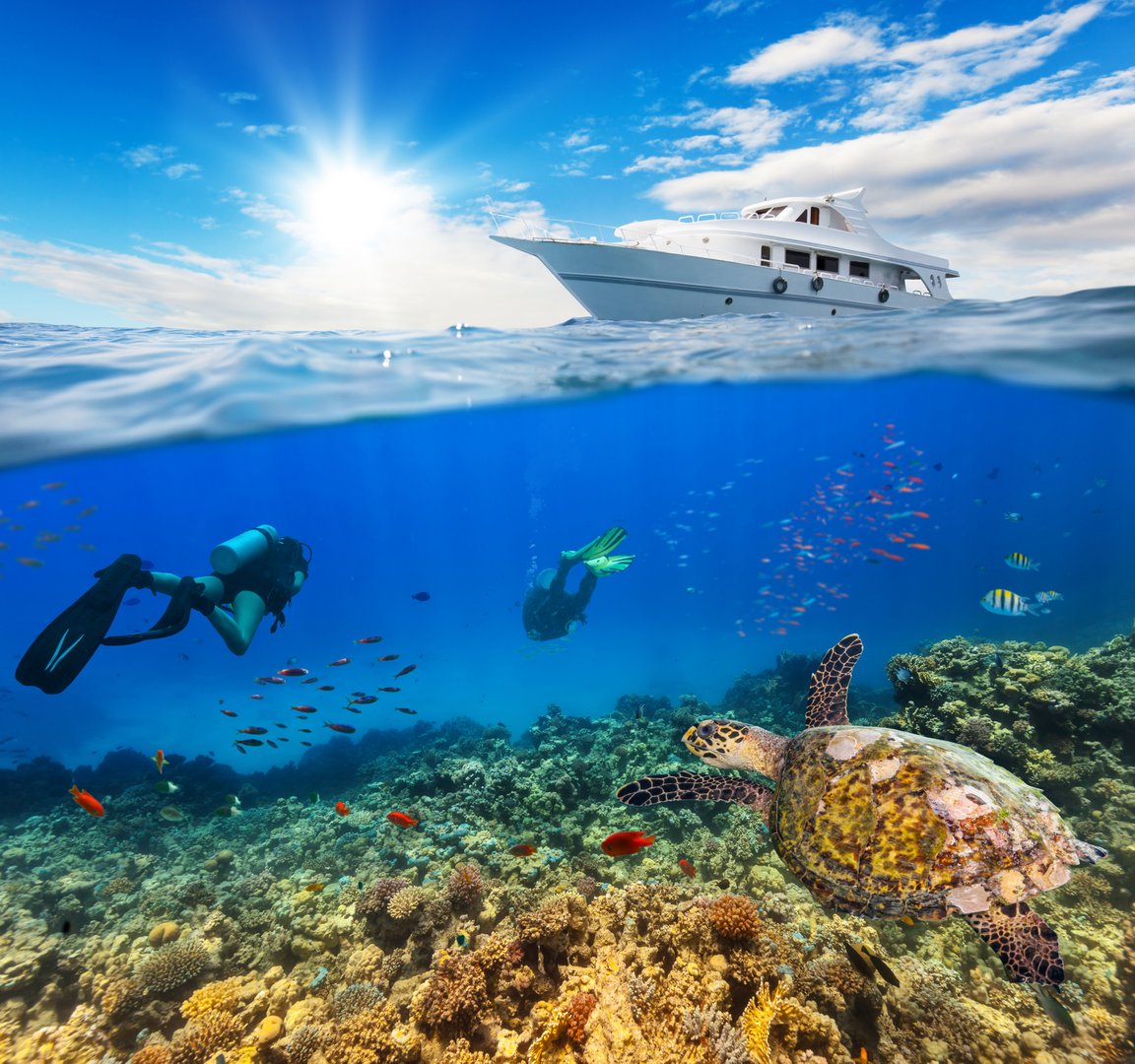 Underwater view of coral reef and scuba divers with horizon and water surface split by waterline. Anchoring yacht on waves. Summer holiday concept. High Resolution