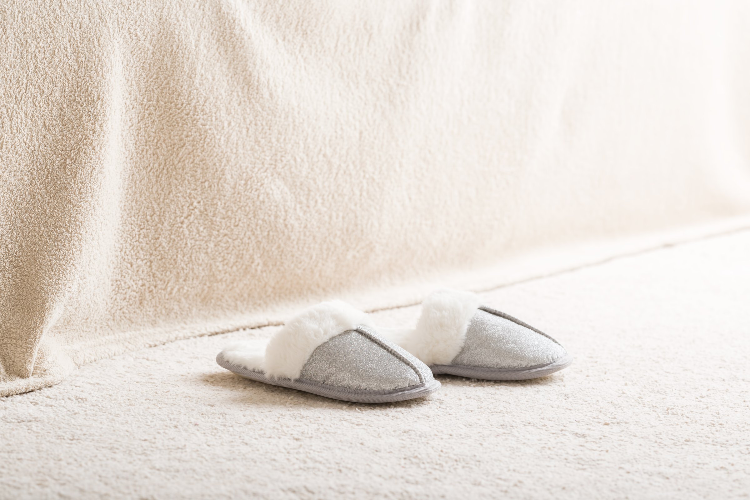 Warm fluffy female slippers on light carpet at home room. Closeup. Side view.
