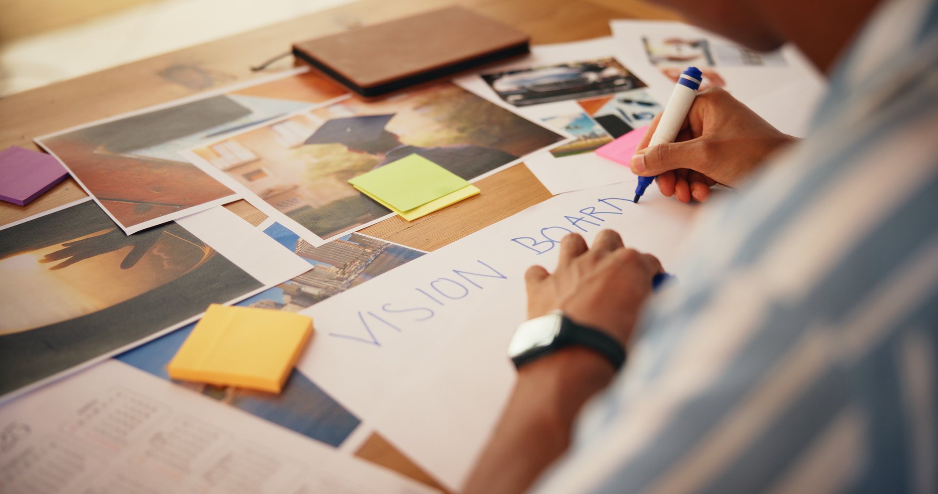 Hands, planning and writing on vision board in home for growth activity, aspirations design and manifestation. Poster, person and pictures for inspiration, progress tracking and personal development