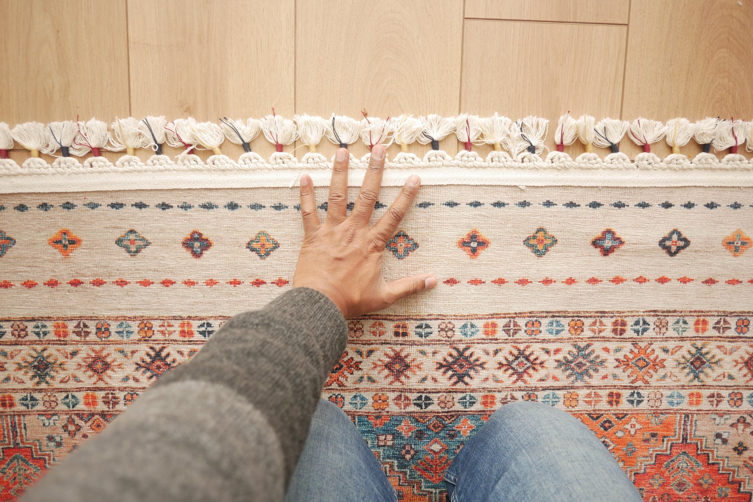 A closeup view of a hand gently resting on the edge of a vibrant, patterned rug