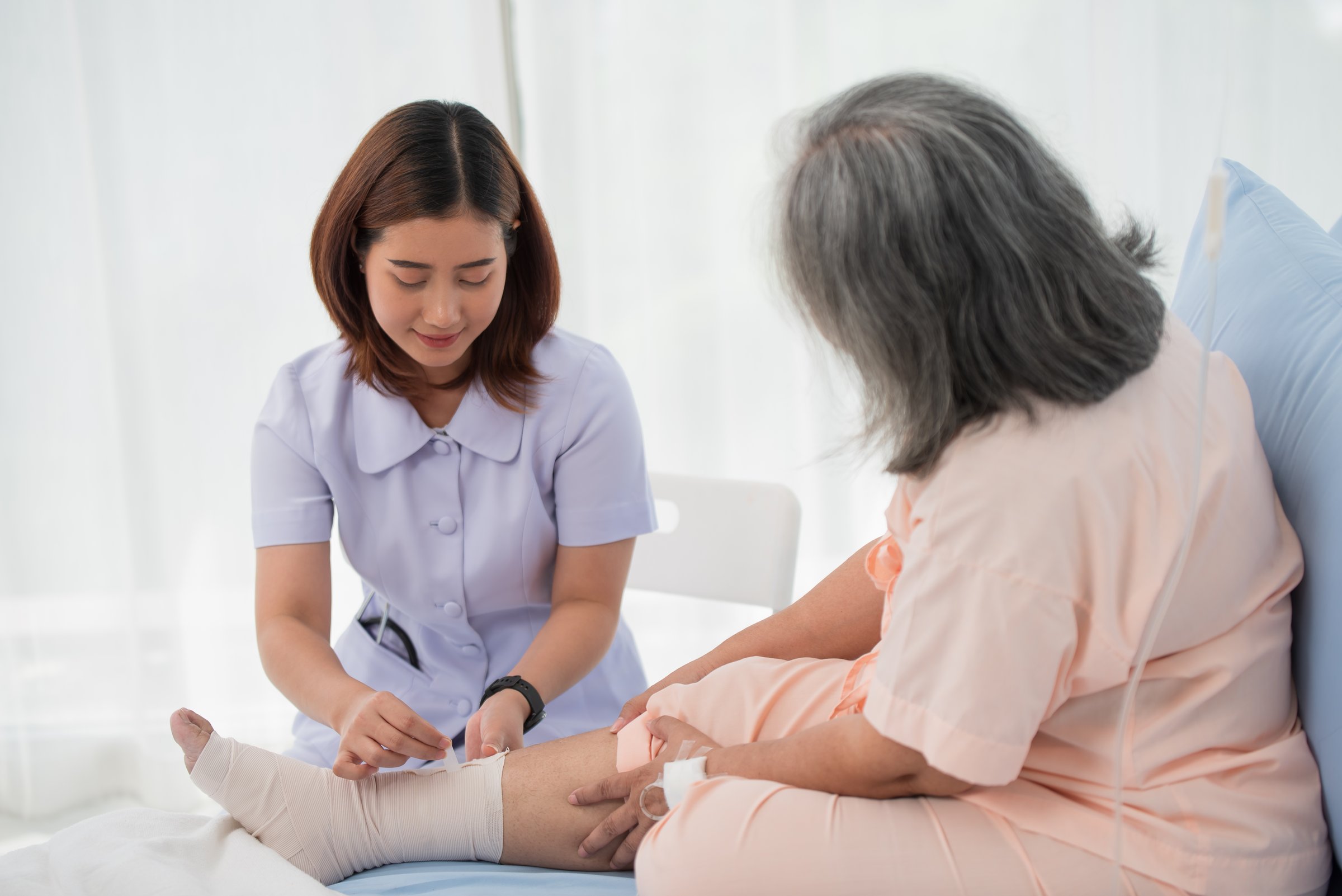 Asian female nurse bandaging foot of elderly woman patient at the hospital