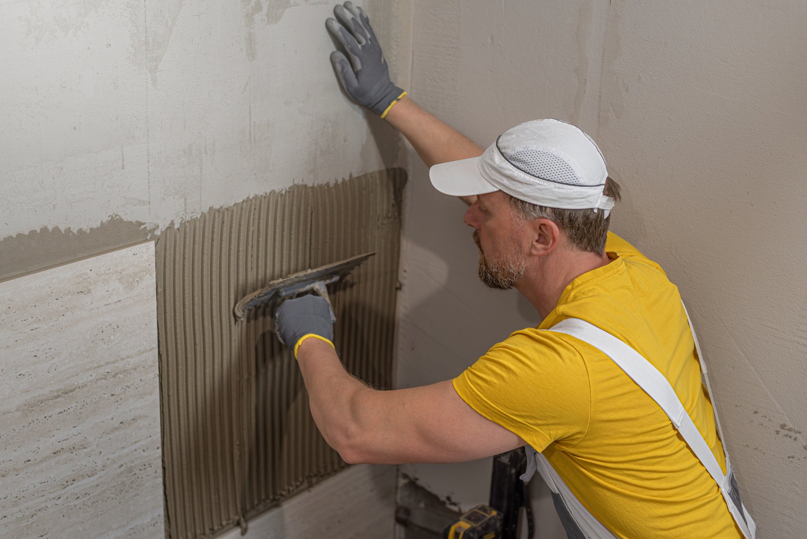 Tiler using notched trowel to spread adhesive