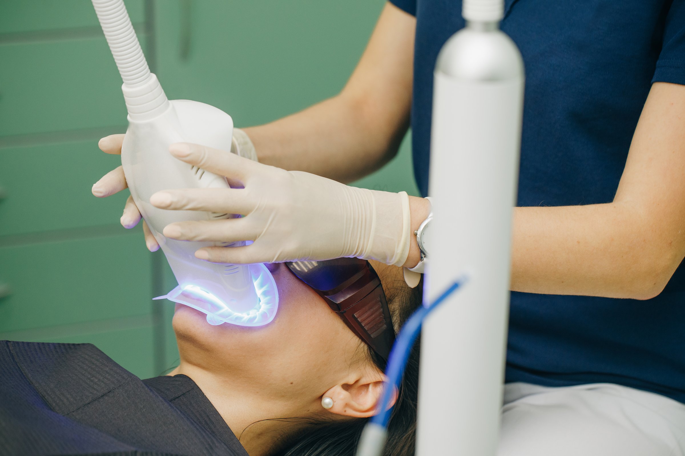Teeth whitening procedure. Powerful light source is directed at patient's mouth to speed up the process. Dentist stomatologist whitening teeth for patient in medicine dental clinic with lamp.
