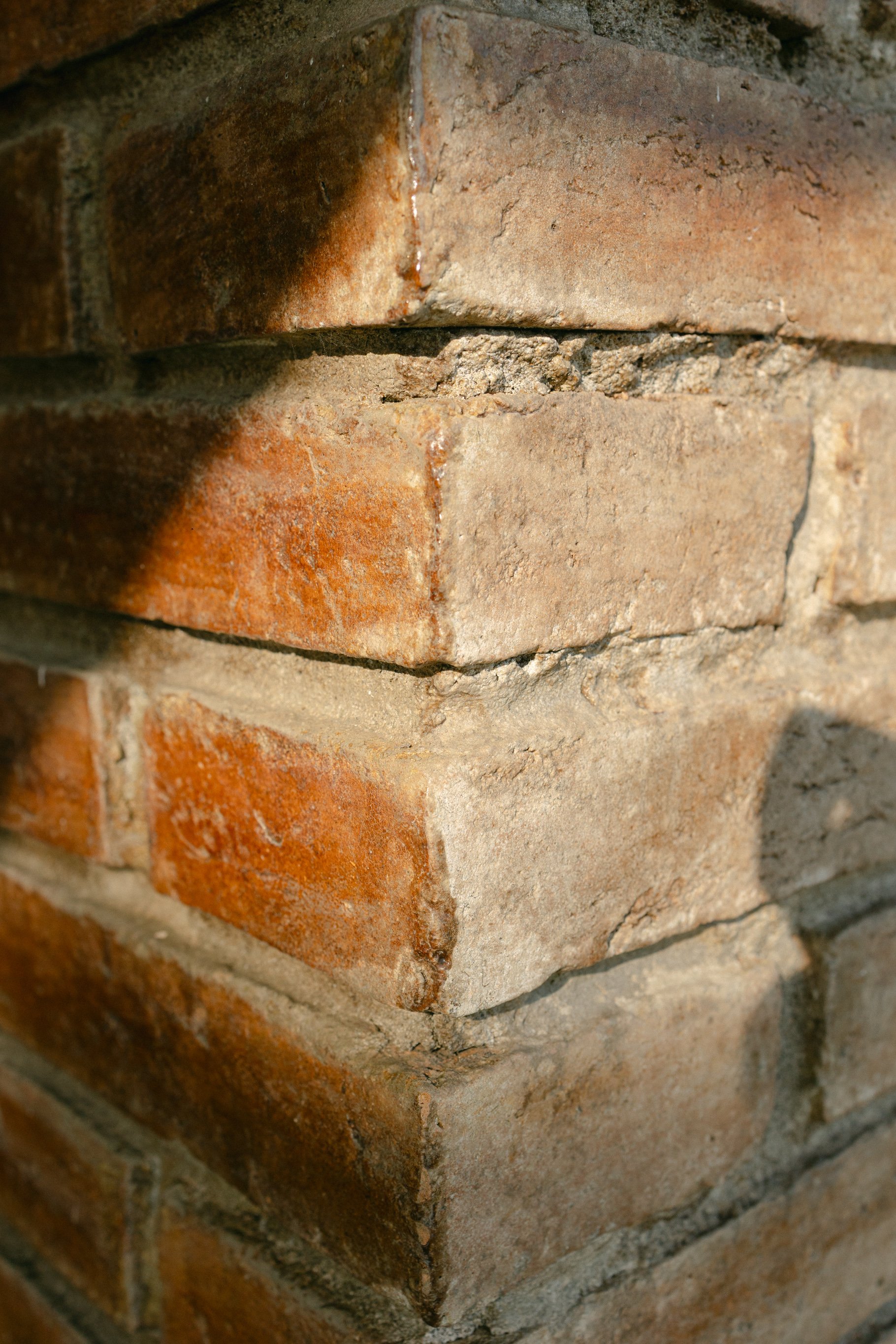 Close-up of a corner of a brick wall with sunlight casting a shadow on the surface, highlighting the texture and mortar.