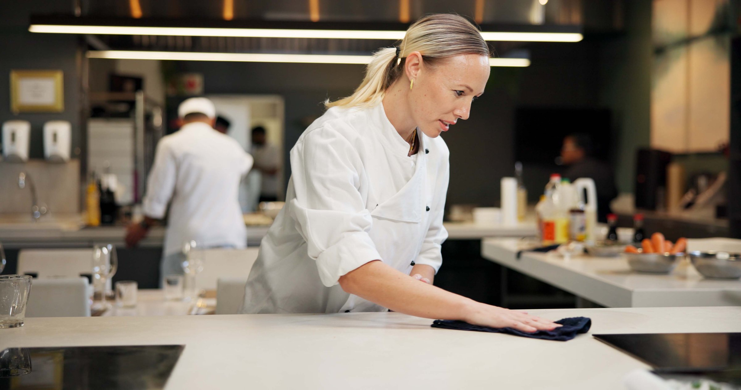 Woman, cleaning and chef wipe counter for dinner rush prep, hygiene and bacteria removal. Dust, person and employee in kitchen, cloth or restaurant with sanitation, disinfection or hospitality policy
