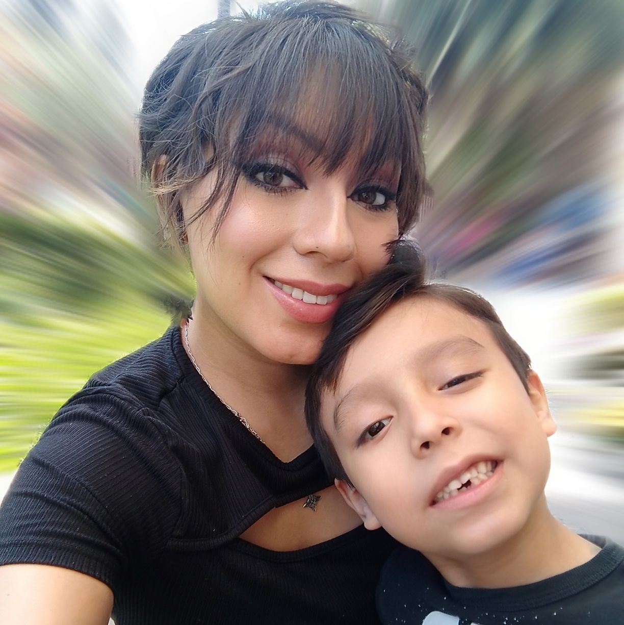 Woman and young boy smiling, with a blurred background, outdoor setting.