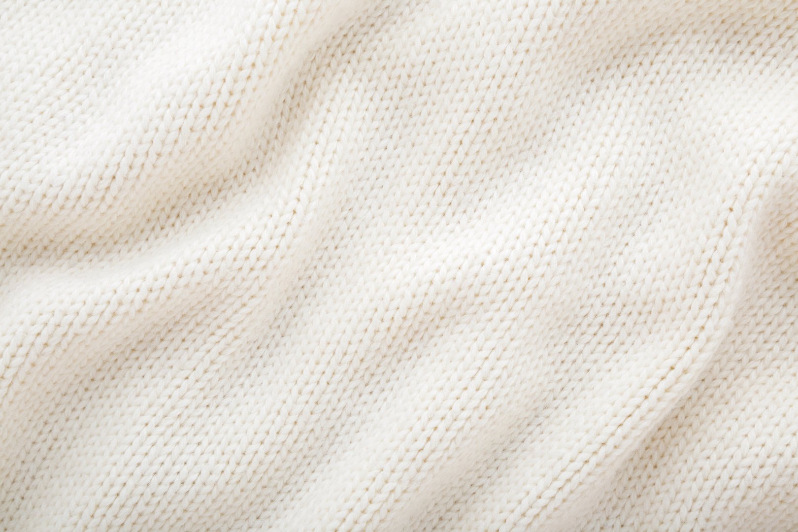 Light white wavy soft knitted fabric background. Closeup. Top down view.