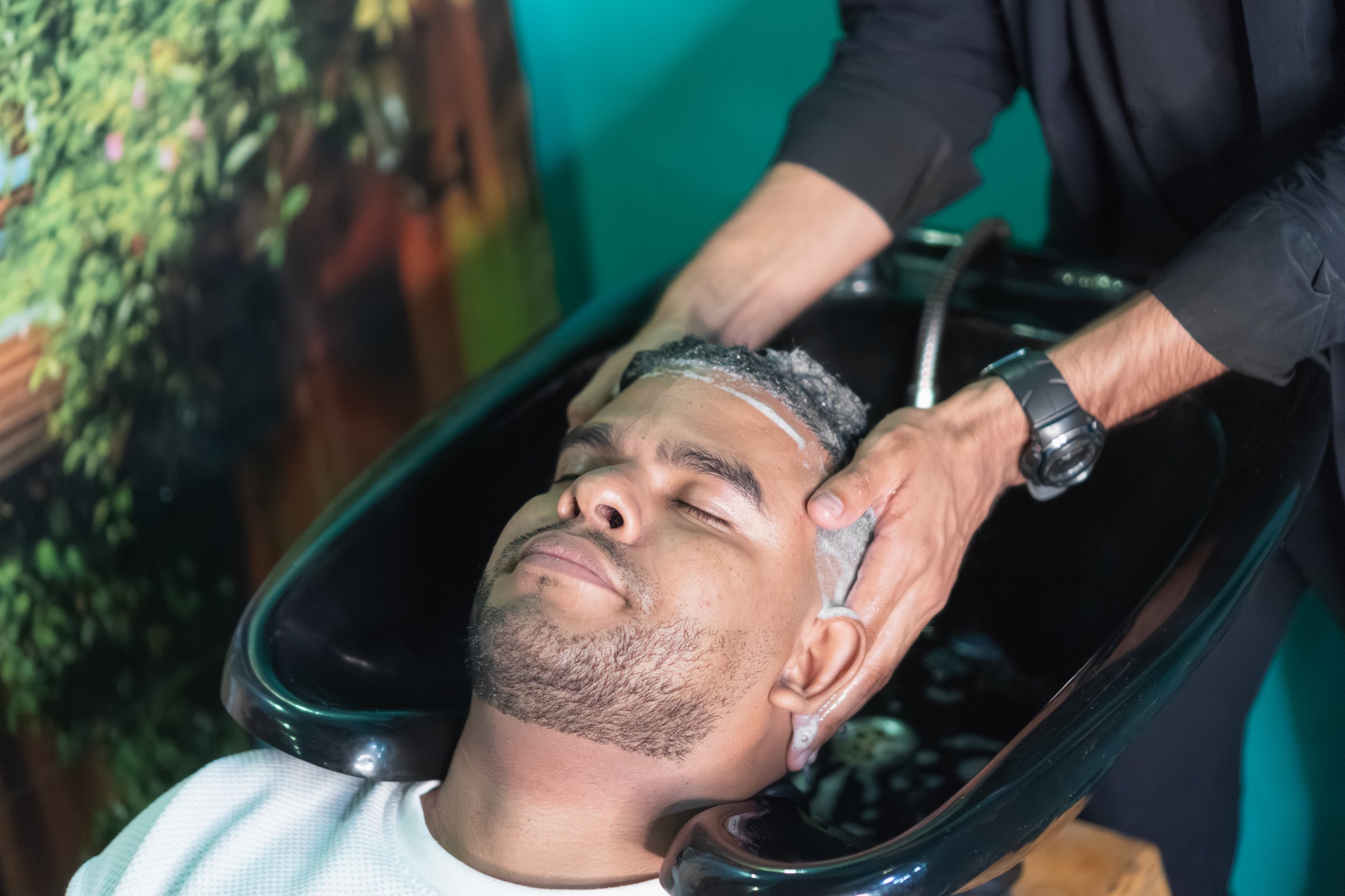 Hairdresser washing a relaxed male client's hair with shampoo in a beauty salon sink