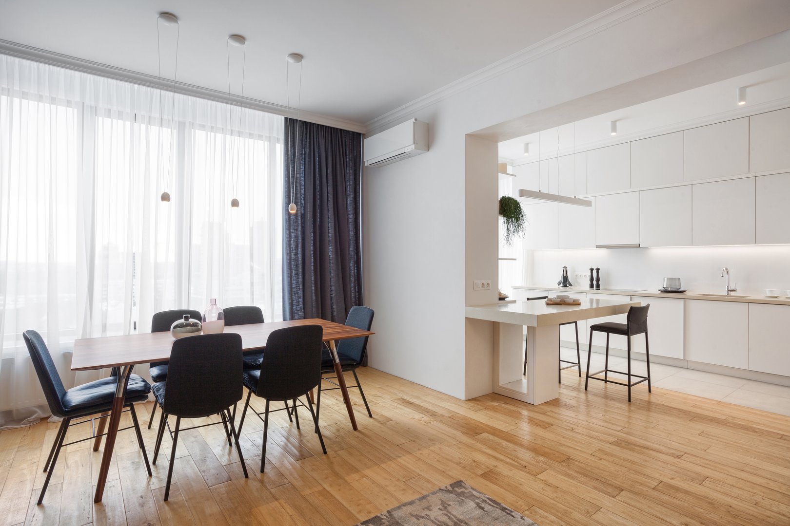 contemporary kitchen and living room interior in flat studio. dining table and chairs on wooden laminate floor against window with curtains