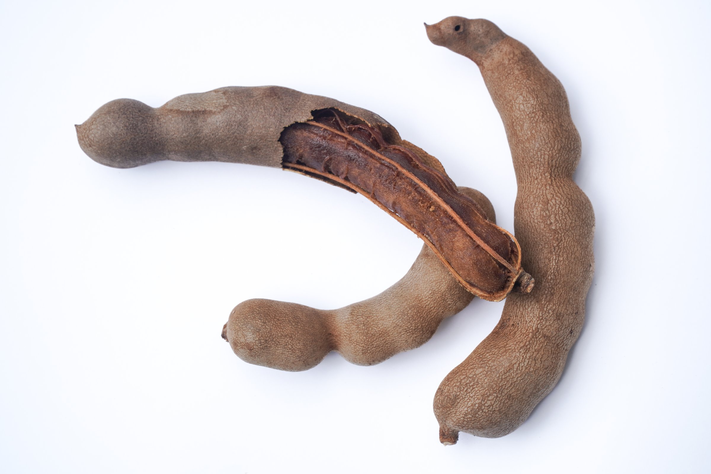 Natural tamarind pods are showcased on a clean white background, with one pod peeled back to display its sticky, edible fruit pulp
