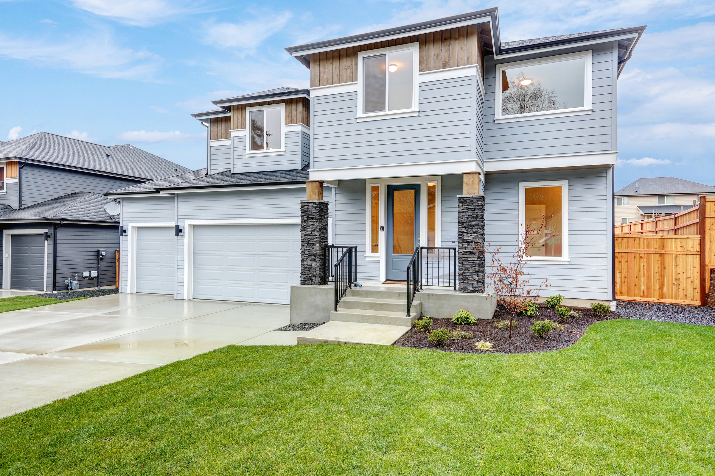 Hew luxury home exterior featuring three Car Garages, pale blue siding and covered porch accented with stone columns. Northwest, USA