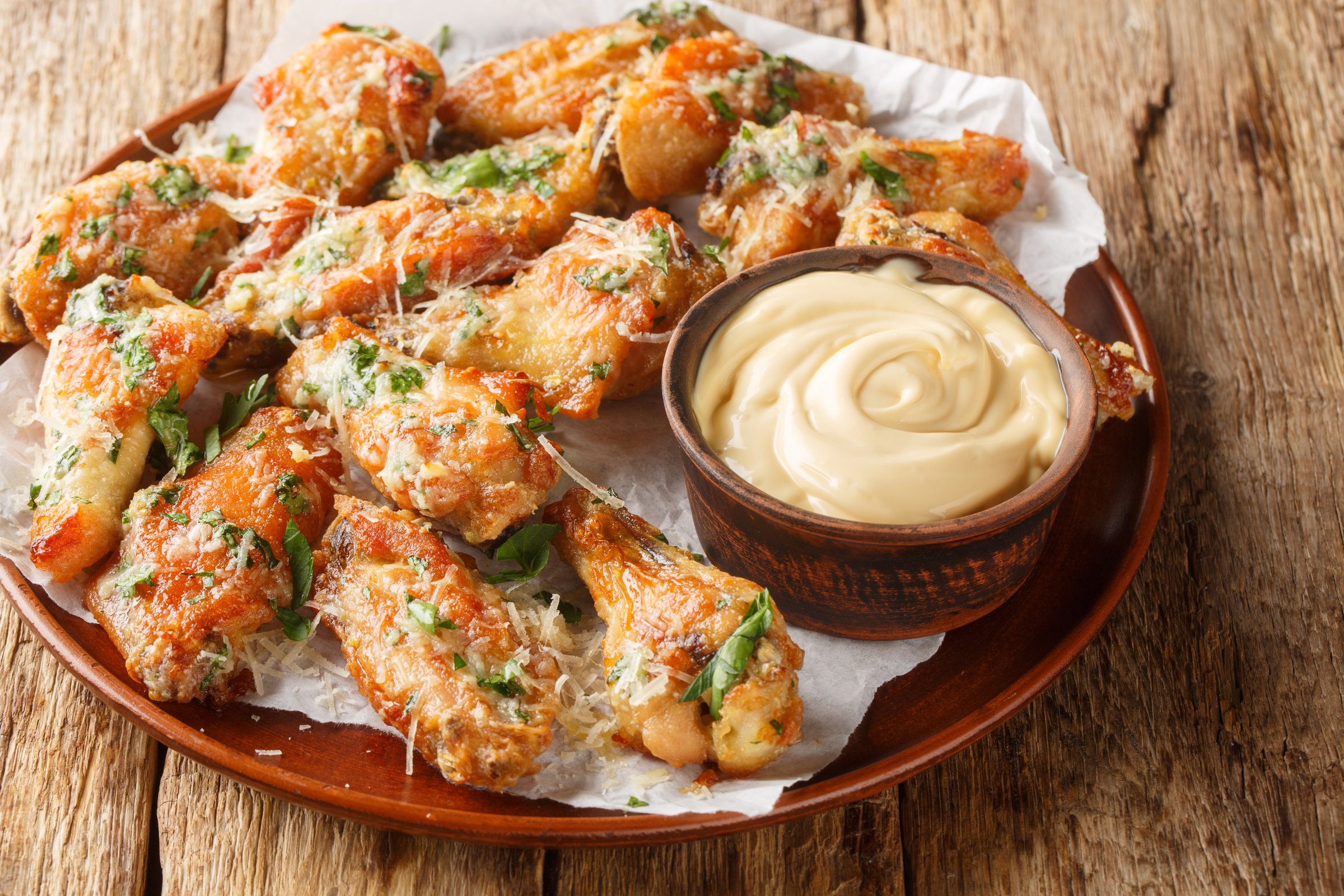Garlic parmesan baked chicken wings served with mayonnaise close-up in a bowl on the table. Horizontal