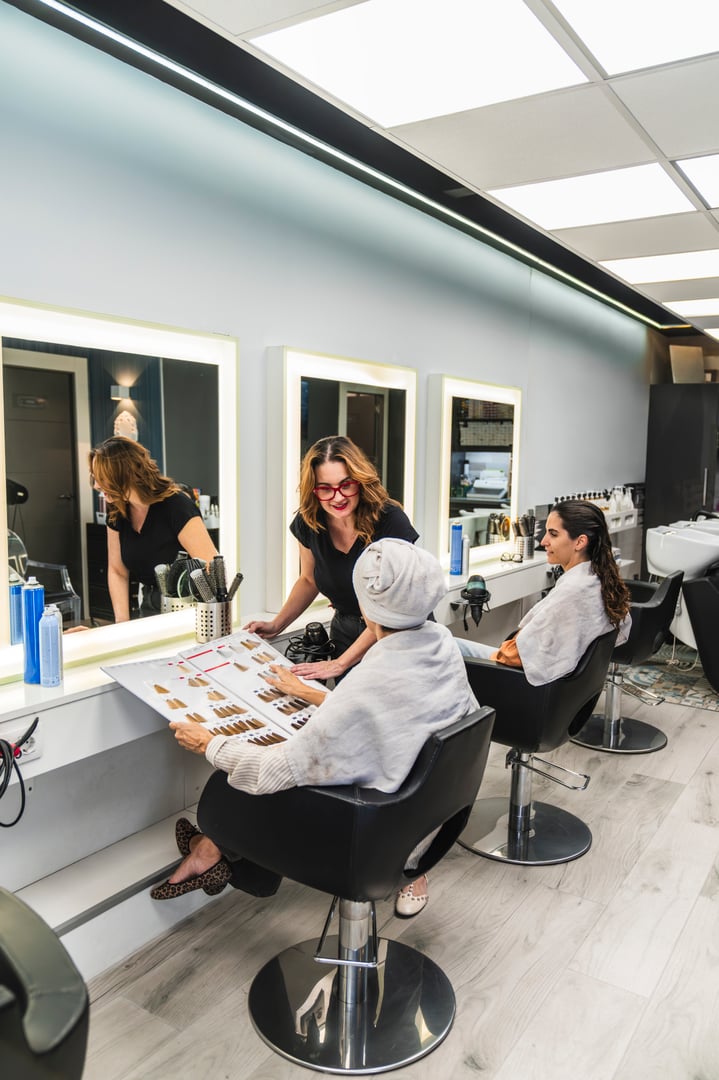 Professional hairdresser assisting a mature adult client selecting a hair dye from a color chart in a modern beauty salon