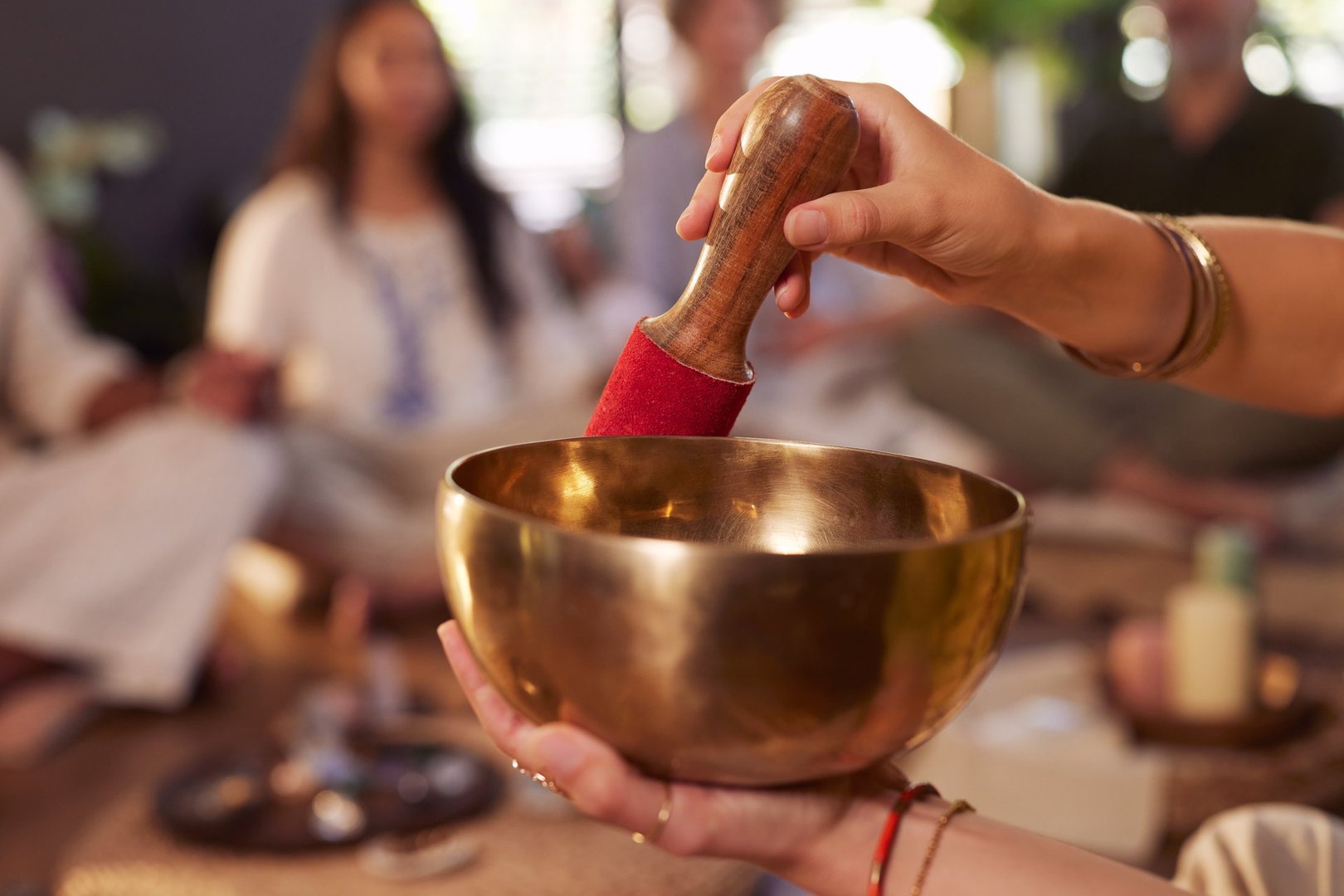 Close up of woman's hand playing singing bowl during group meditation session with copy space. Brass sound bowl used for healing and energy work at indoor wellness retreat. Peaceful spiritual practice with focus and intention with tibetan bells.