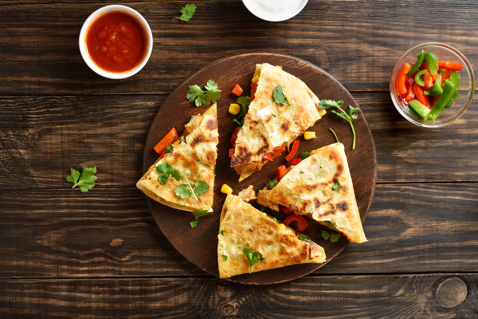 Delicious chicken quesadilla with fresh vegetables on serving board on brown wooden background. Top view, flat lay