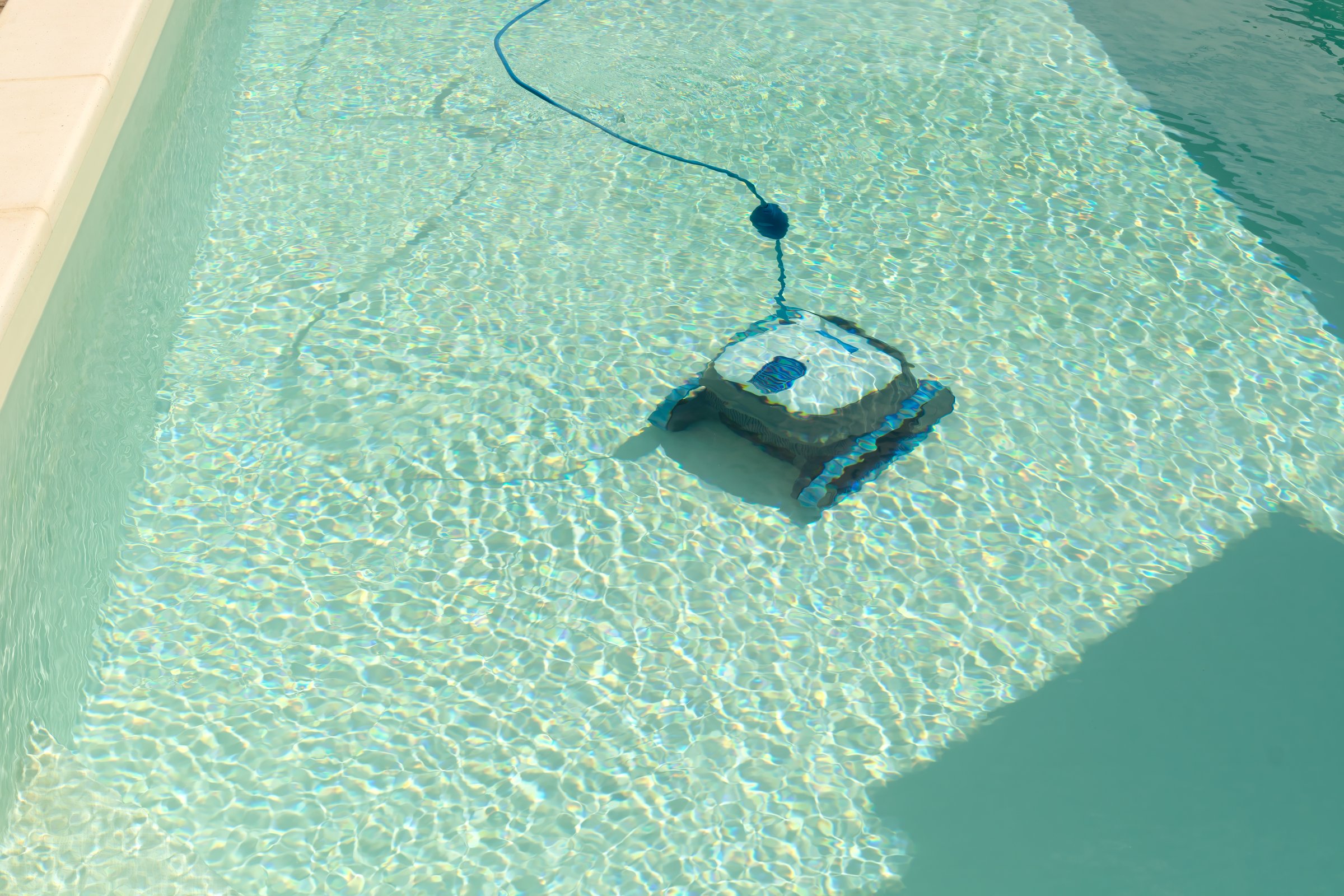The robot pool cleaner cleans the bottom of the pool with clean water on a sunny summer day. The concept of cleaning swimming pools in hotels, resorts and country houses.