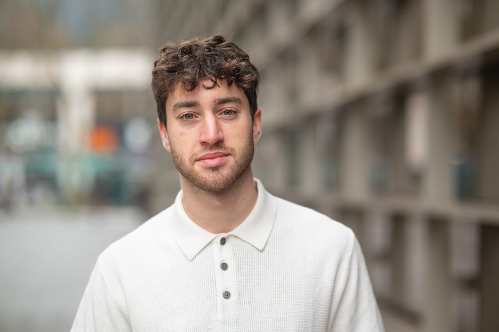 Young man with curly hair and light eyes looking at camera in an urban environment