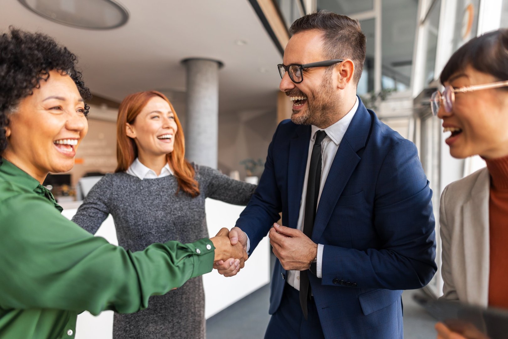 Colleagues in a professional office environment expressing happiness and cooperation through handshakes and laughter, showcasing the essence of teamwork and mutual respect in a business setting.