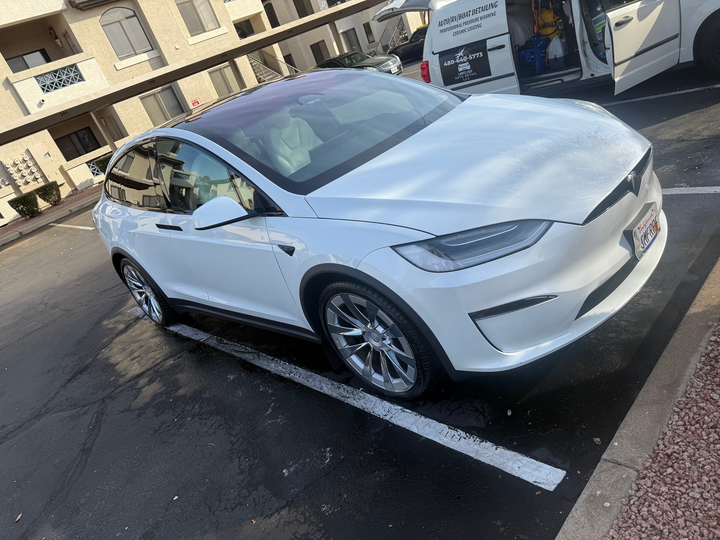 A white Tesla Model X parked in a residential parking lot next to a van.