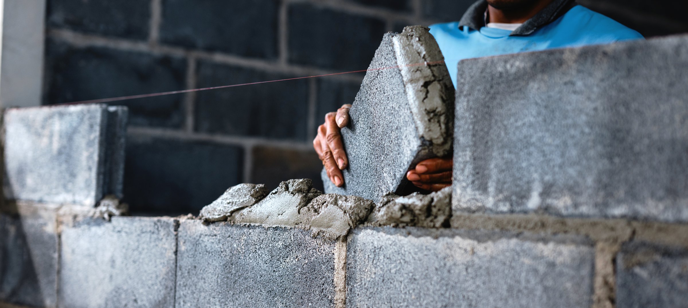 man is cutting a brick with a wire. The brick is grey and the man is wearing a blue shirt