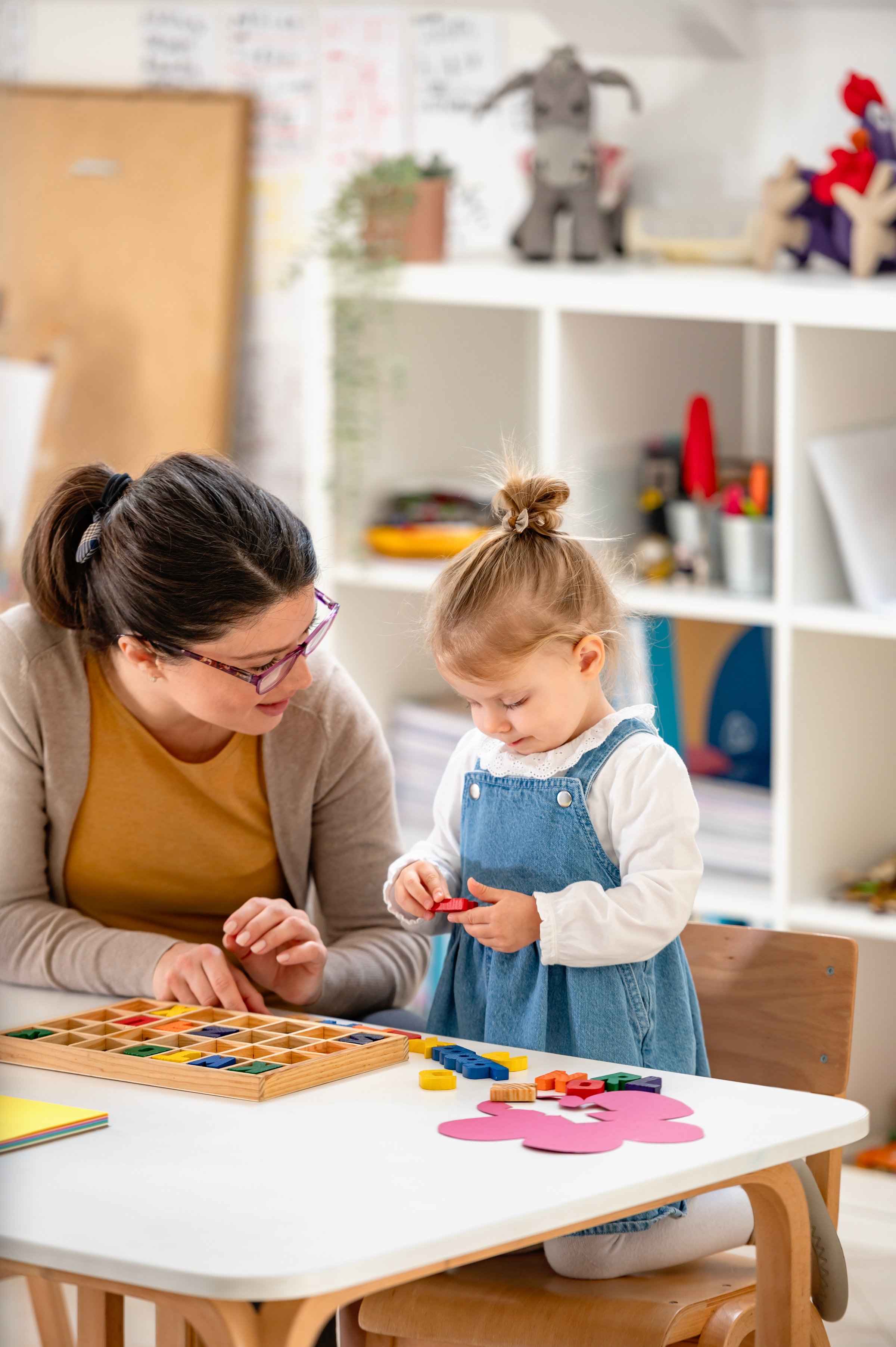 A young woman and a little girl engage in creative play with colorful building blocks in a bright classroom, fostering learning, fine motor skills, and early childhood development