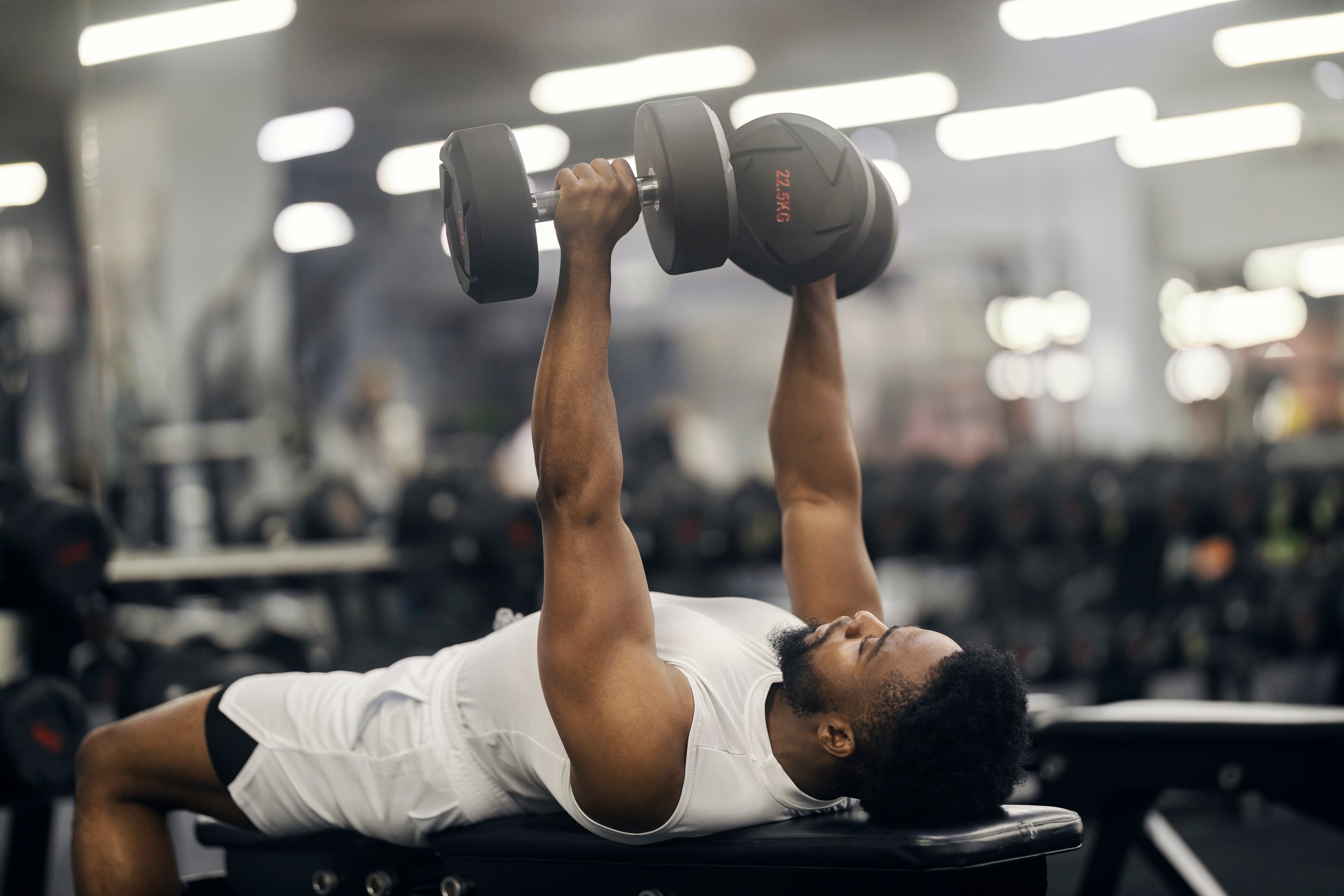 Young adult man performing a chest press exercise with heavy dumbbells, focusing on strength training and fitness in a gym