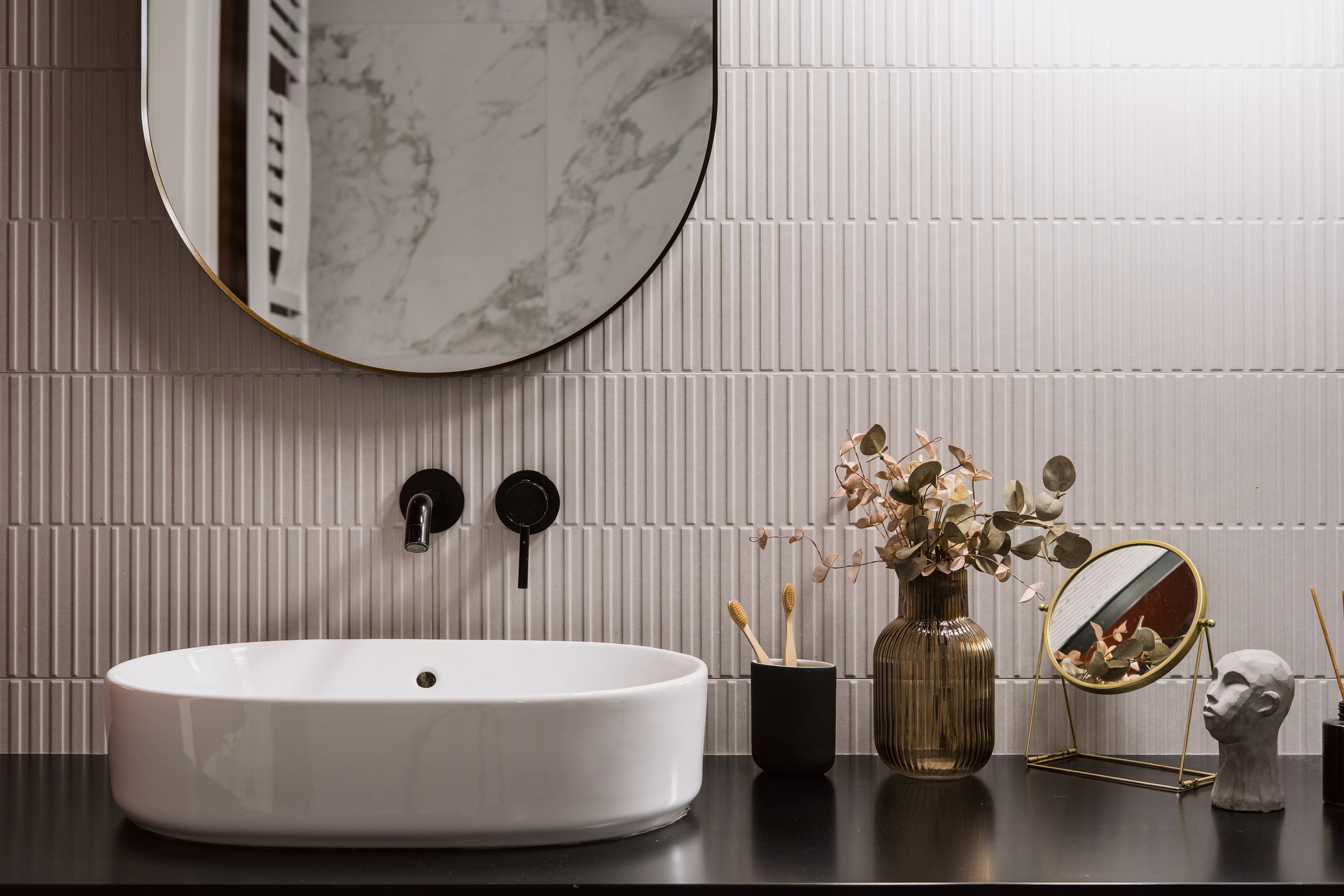 A clean and minimalist bathroom features a white sink with a round mirror above. Decorative vases and plants add a touch of elegance to the contemporary space in hotel room