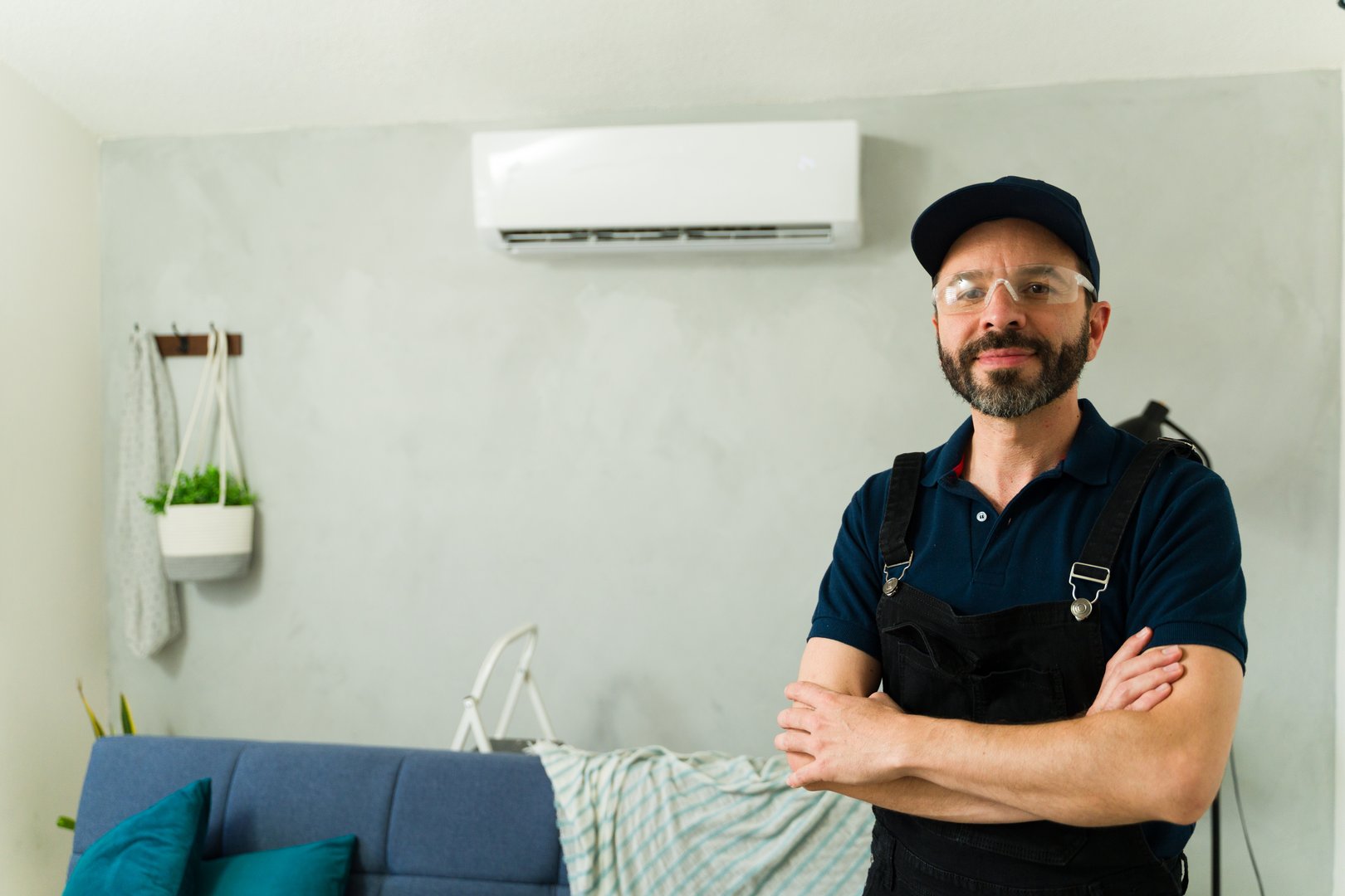 Confident hvac technician with arms crossed in a modern living room, installing or repairing a mini split air conditioning unit