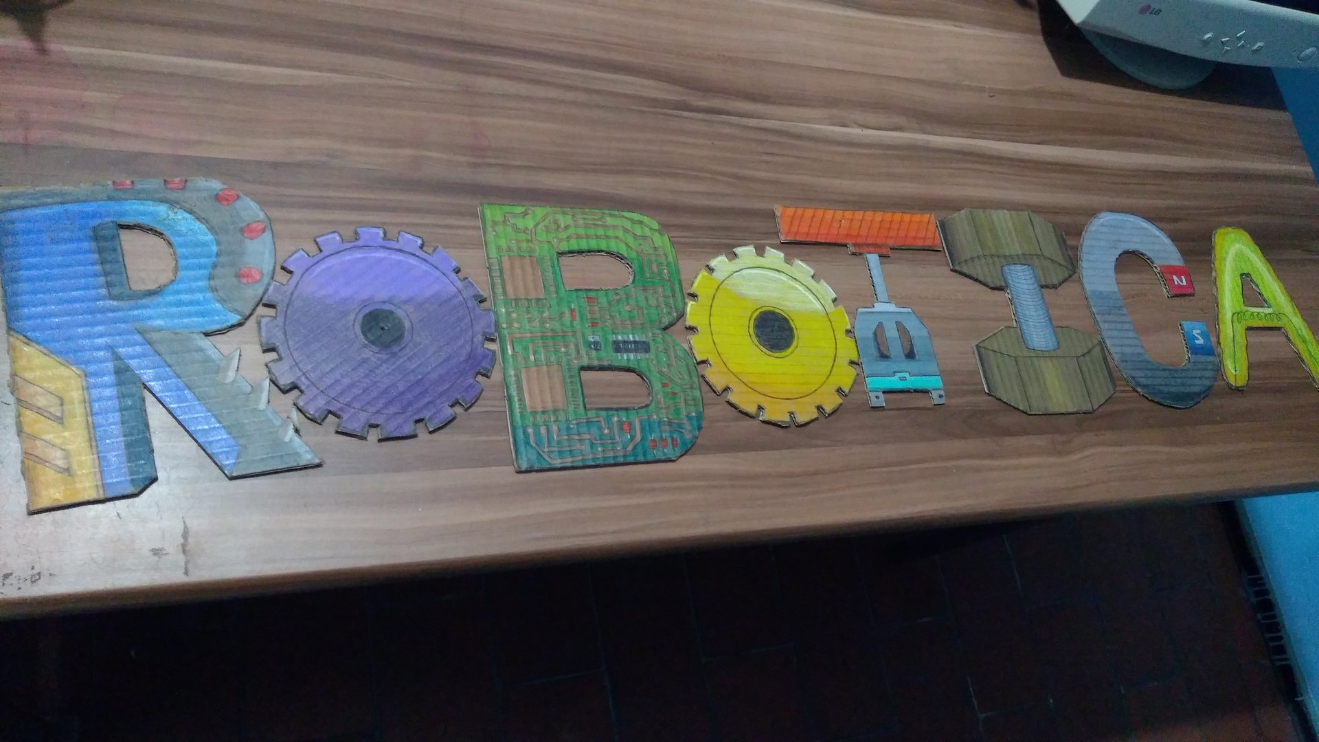 Colorful letters spelling 'ROBOTICA' with each letter designed in a mechanical or technological theme on a wooden table.