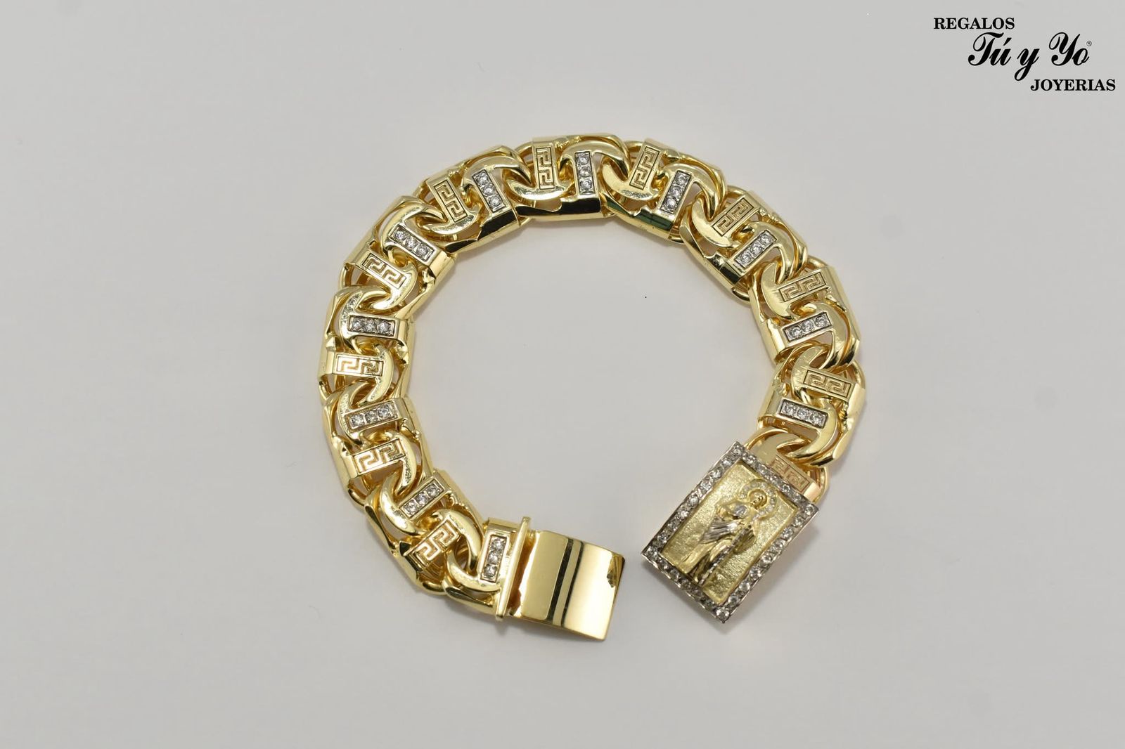 Gold bracelet with intricate links and a rectangular clasp featuring an engraved relief design, displayed on a plain background.