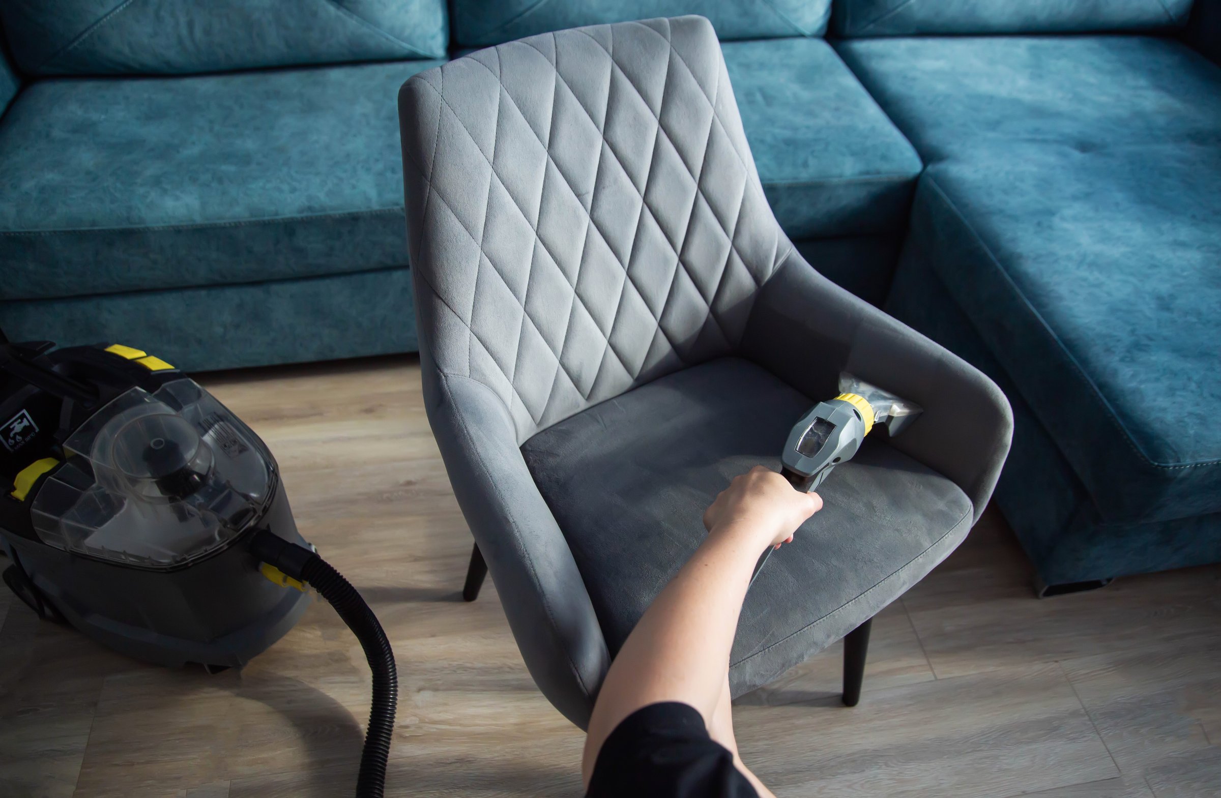 The hands of a girl with a washing vacuum cleaner clean and wash the gray upholstery of a soft chair from dirt. Cleaning services, business. Copy space for text