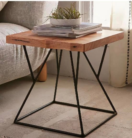 Wooden side table with metal legs, topped with magazines and a small potted plant, next to a sofa in a well-lit room.