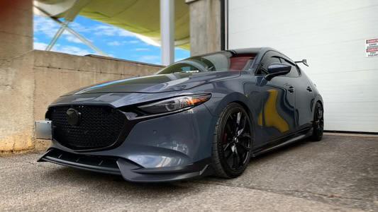 Gray sporty hatchback car with black accents and lowered suspension parked in front of a garage door.